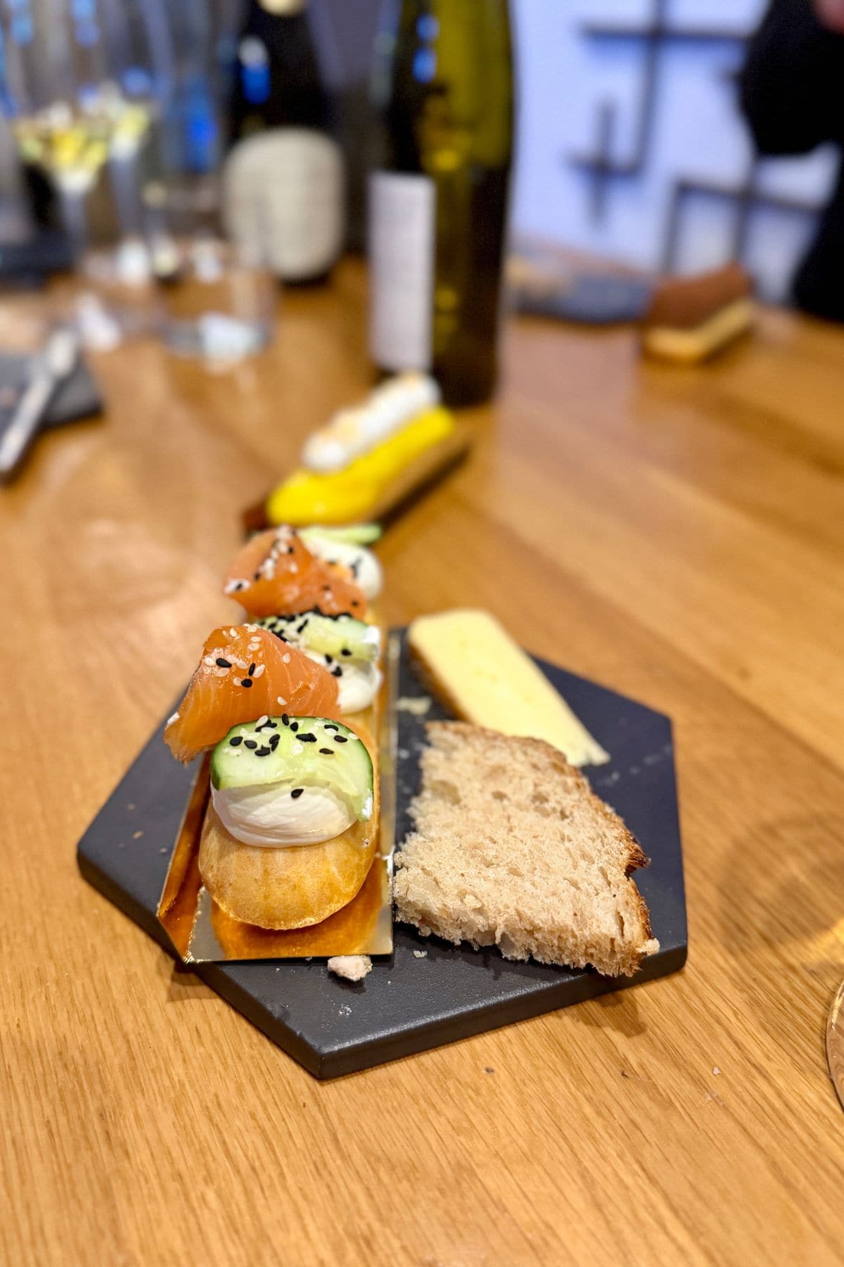 Salmon and cucumber on a savory pastry with a slice of cheese and bread on the side on a black plate.
