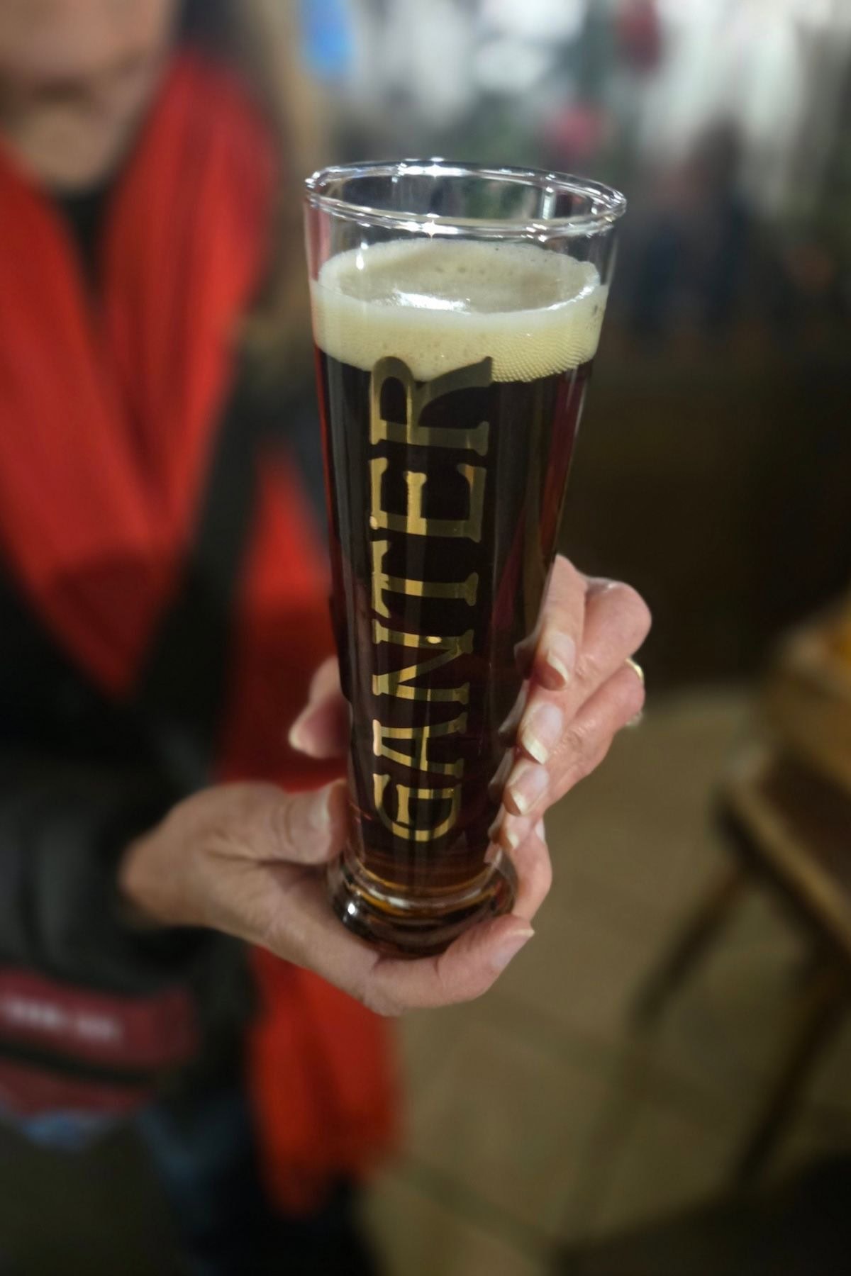 A woman wearing a red scarf holding a tall glass of brown liquid.