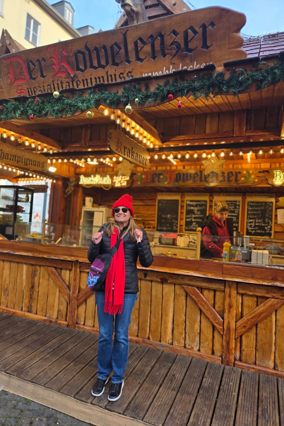 Woman in a red hat and scarf standing in front of a open-air restaurant.