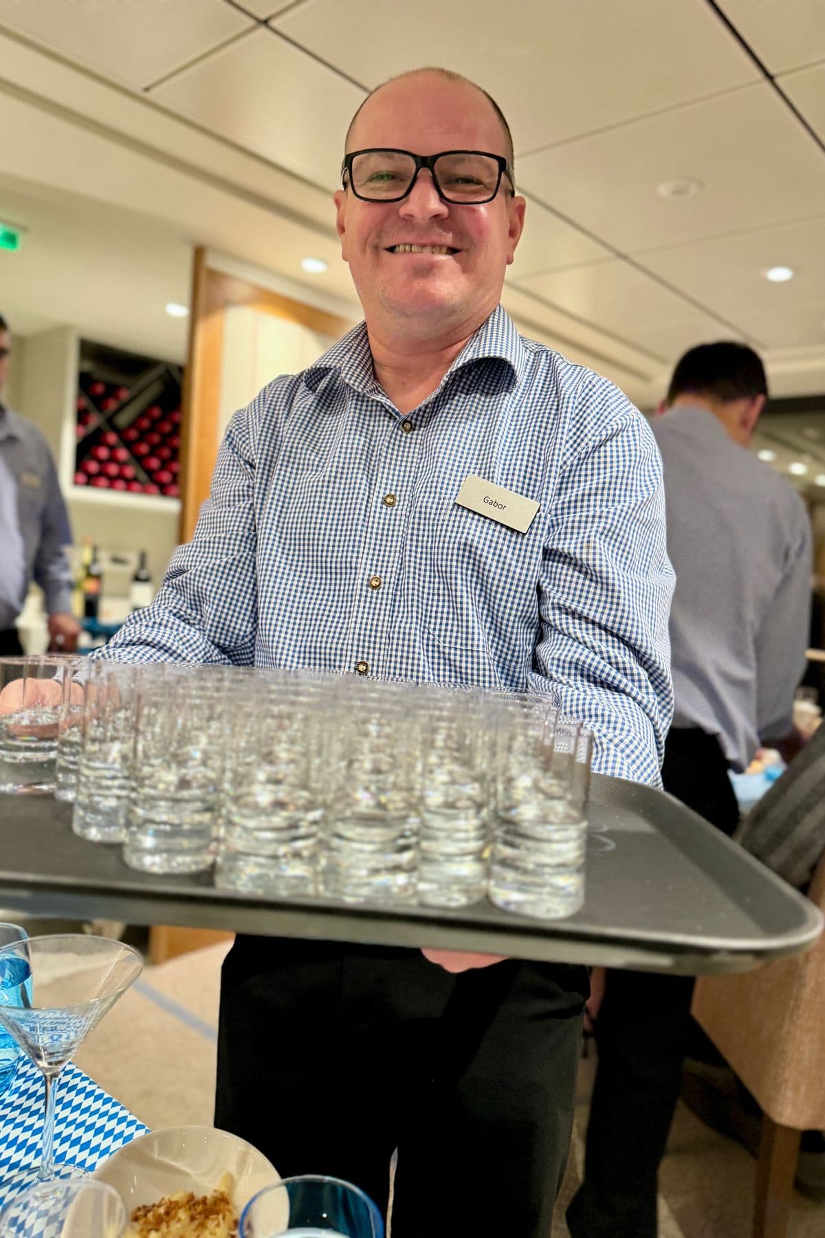 Server holding tray of white liquor in small glasses.