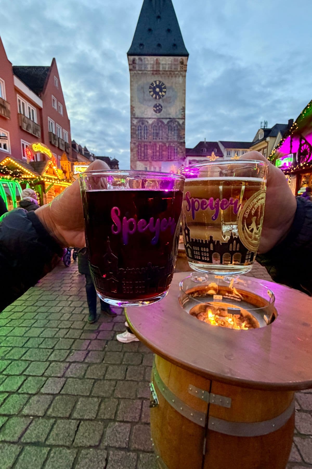 A glass of red liquid and a glass of white liquid touch above a fire pit with a clock tower in the background.