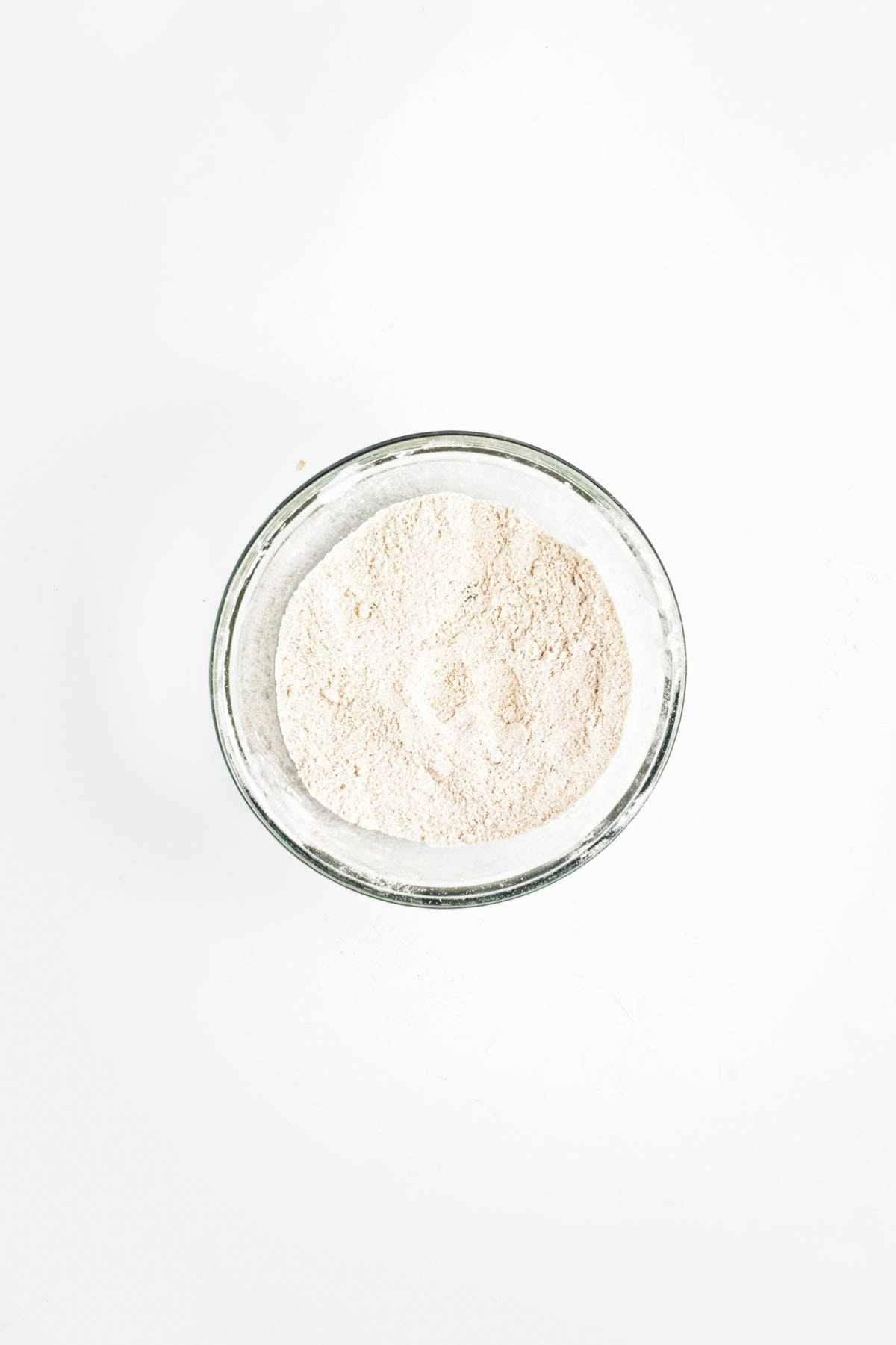 Flour in a glass bowl on a white counter.
