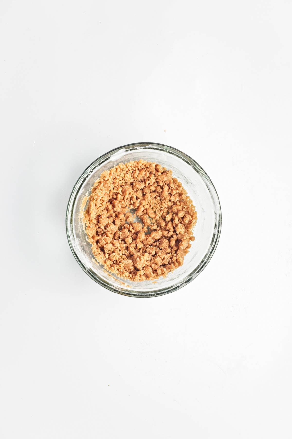 Crumble mixture in a glass bowl on a white counter.