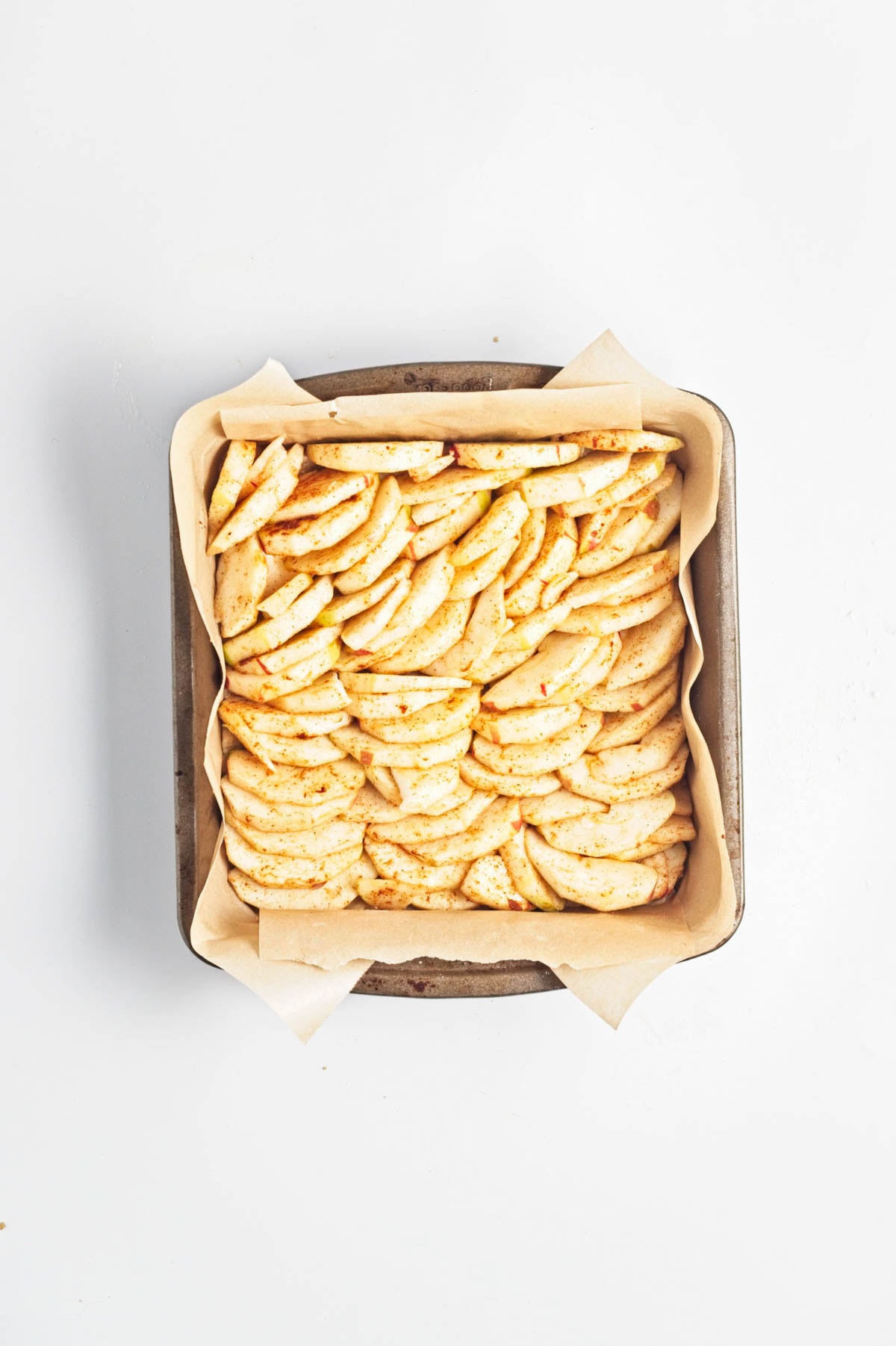 Sliced apples in a parchment paper lined baking dish.