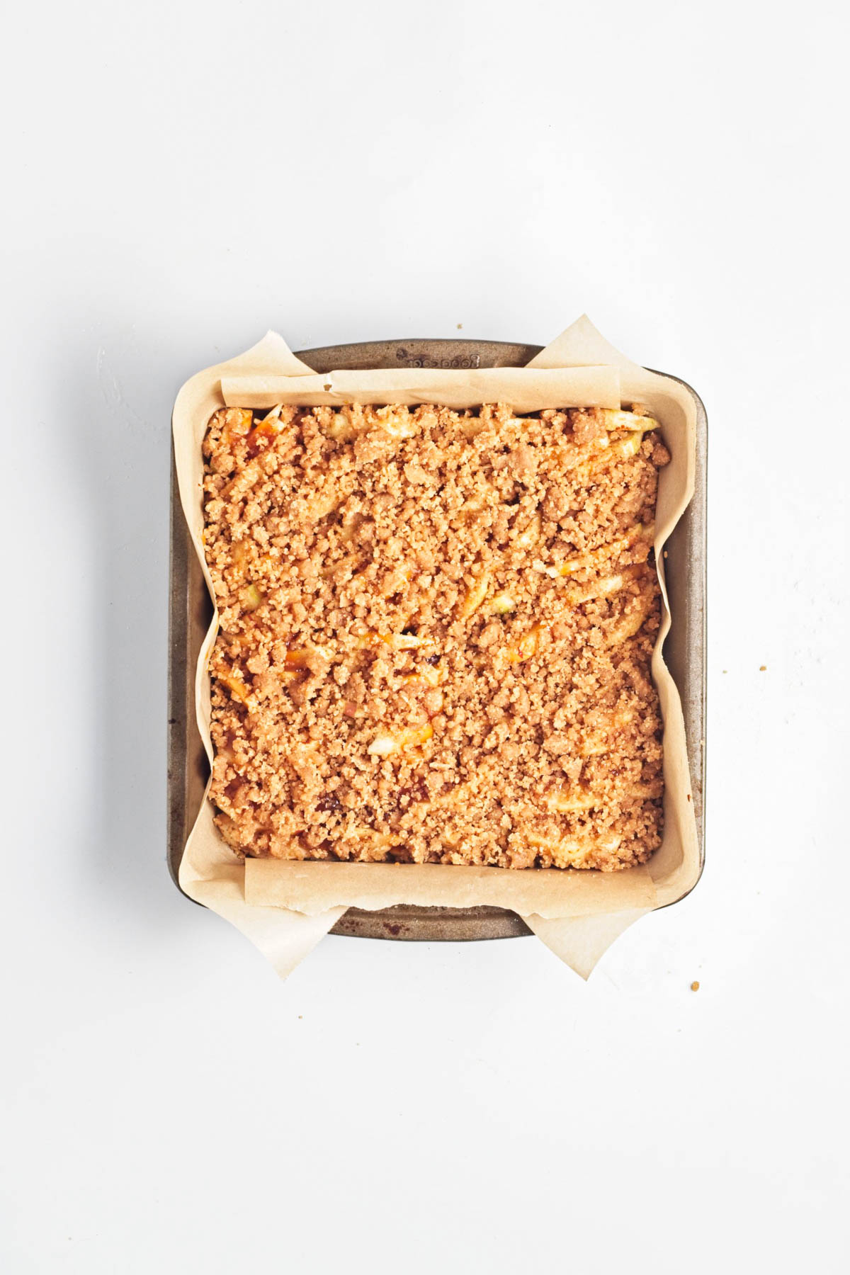 Apple cake with crumble on top in parchment paper-lined baking dish.