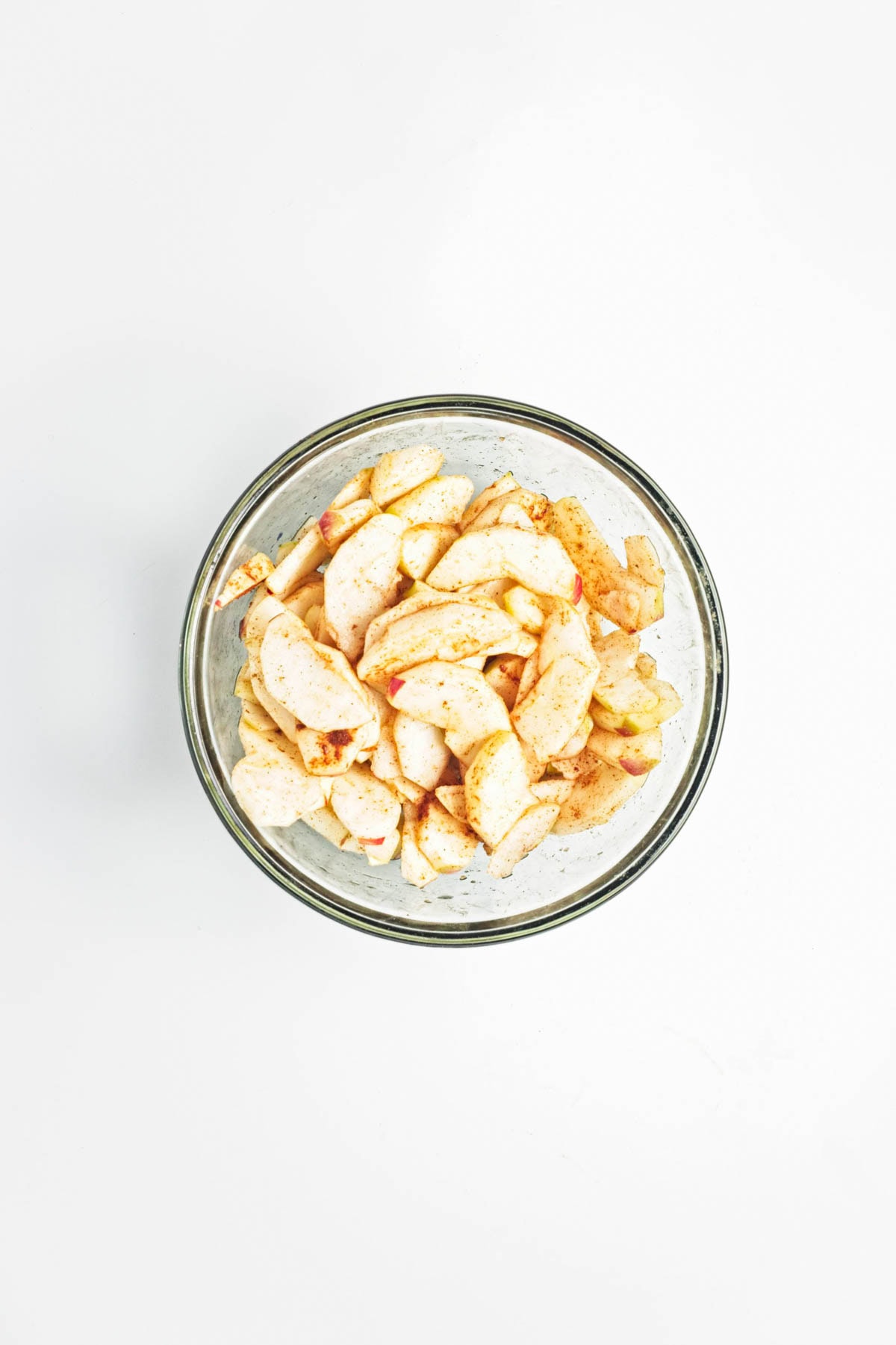 Apples and cinnamon in a glass bowl on a white counter.