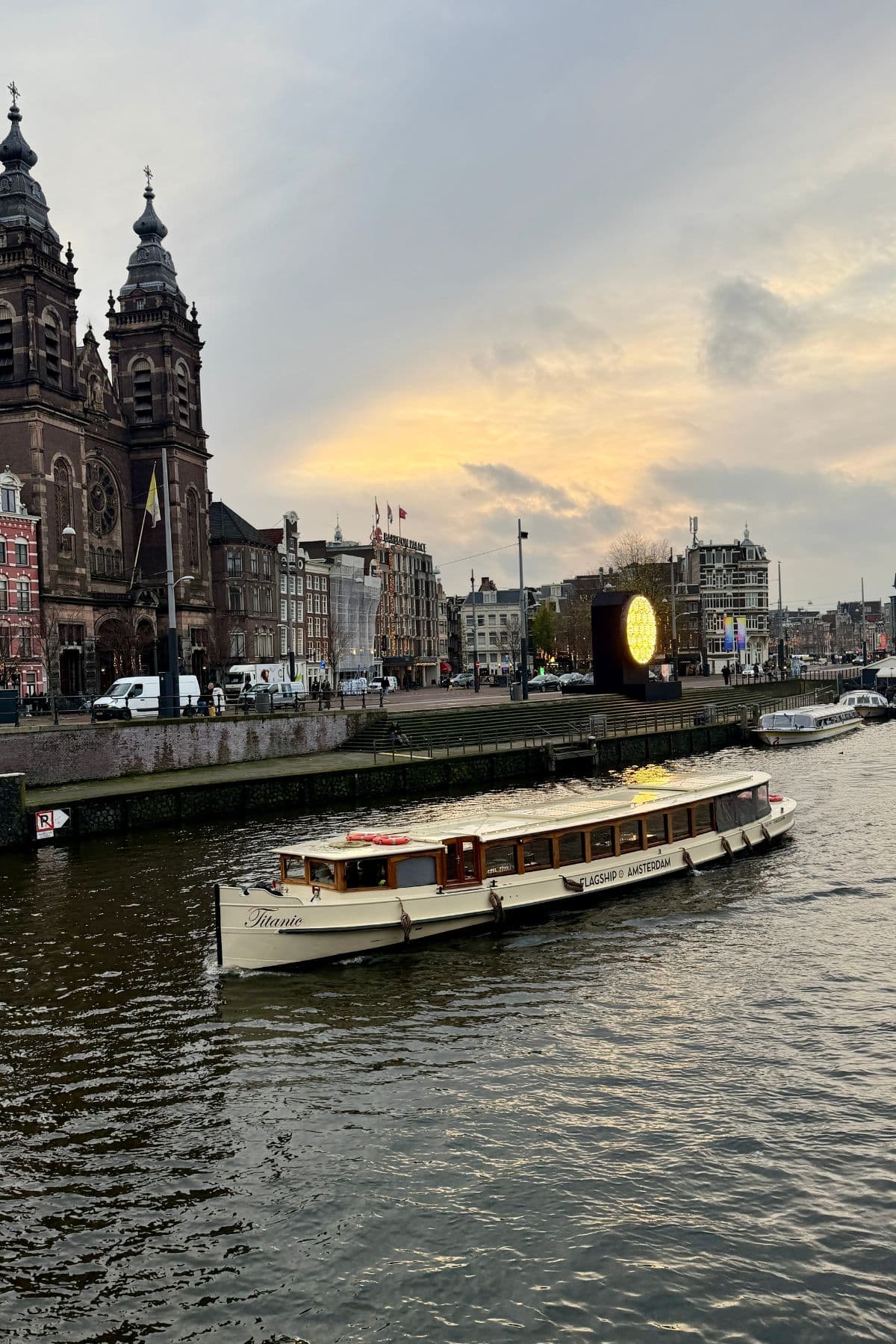 A boat passing by buildings in Amsterdam at sunset.