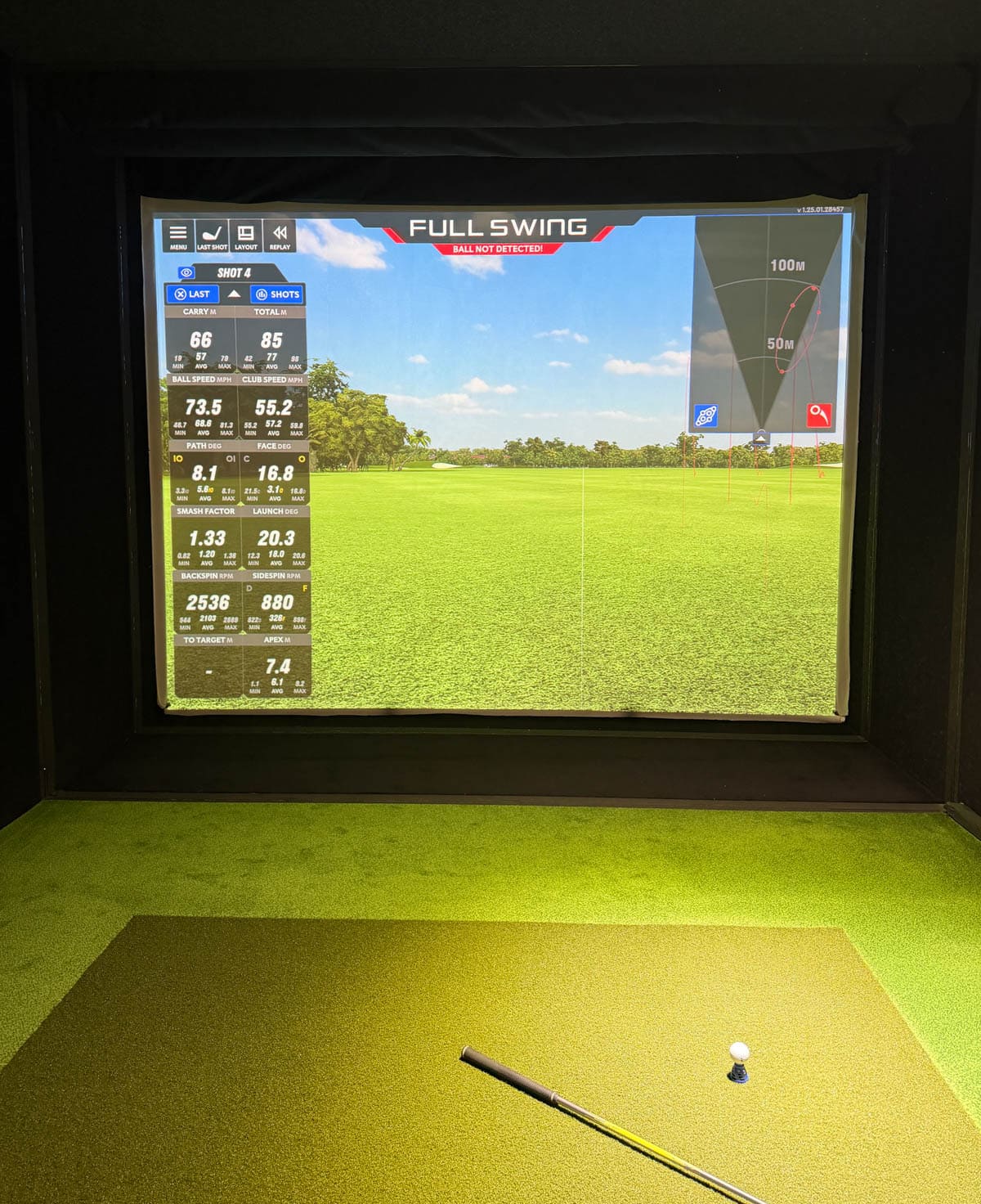 Golf simulator on the wall with gold green in front and clubs on the floor.