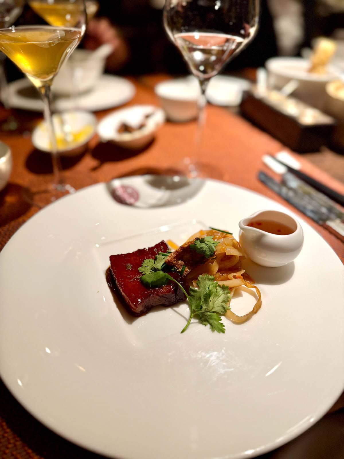 Pork belly on a white plate with a small pitcher of sauce.