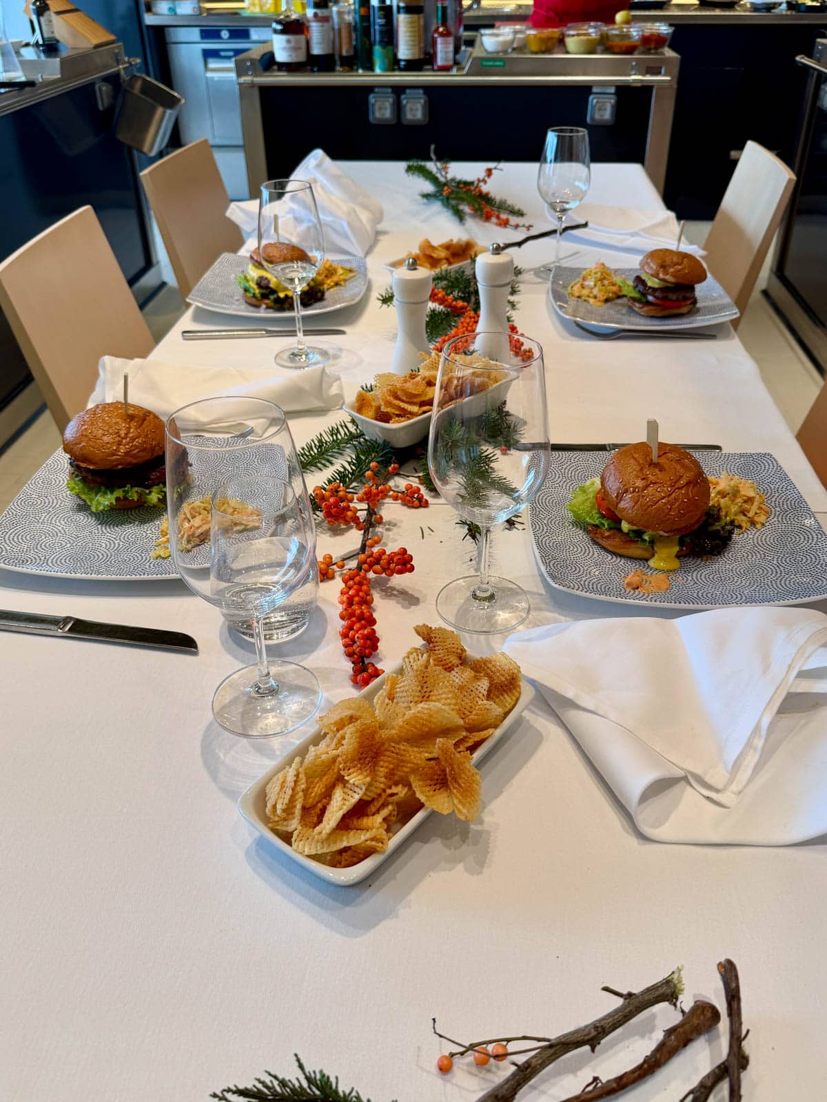 Table set with branches and orange berries with burgers in four place settings.