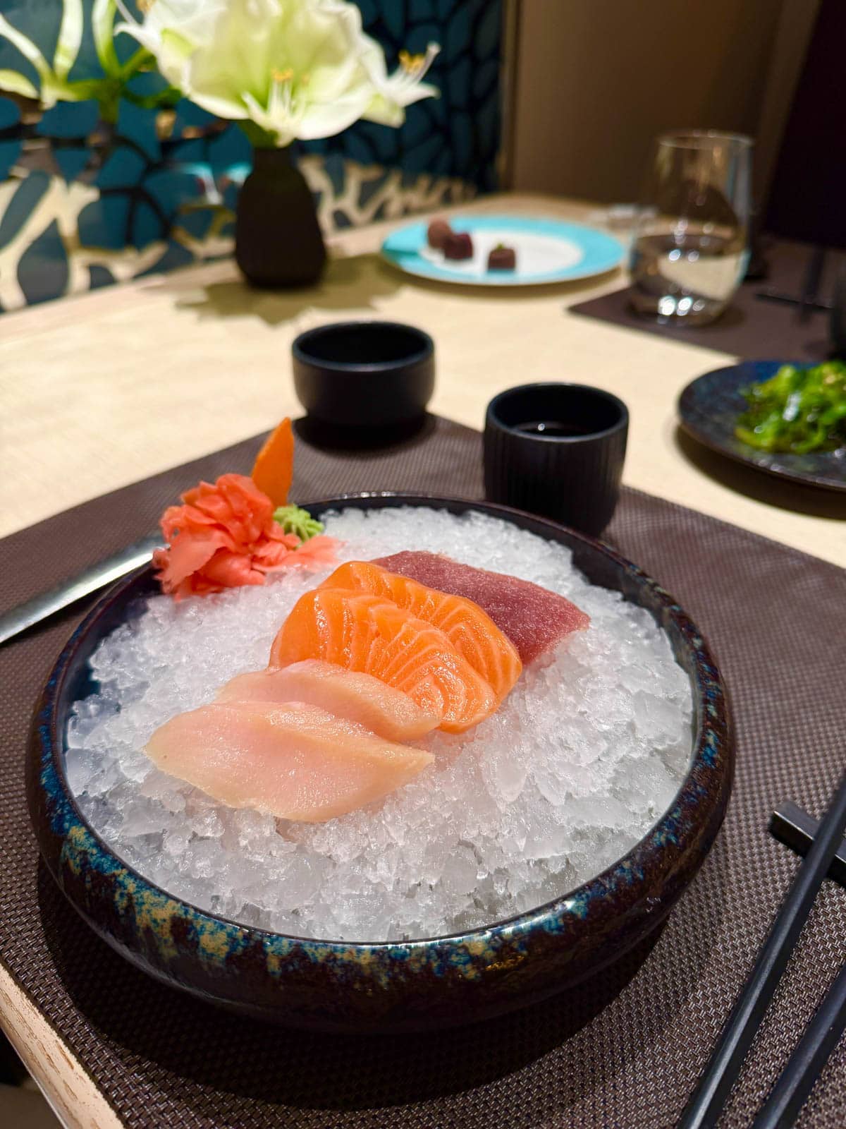 Sashimi on bed of ice in a black bowl with ginger to the side.