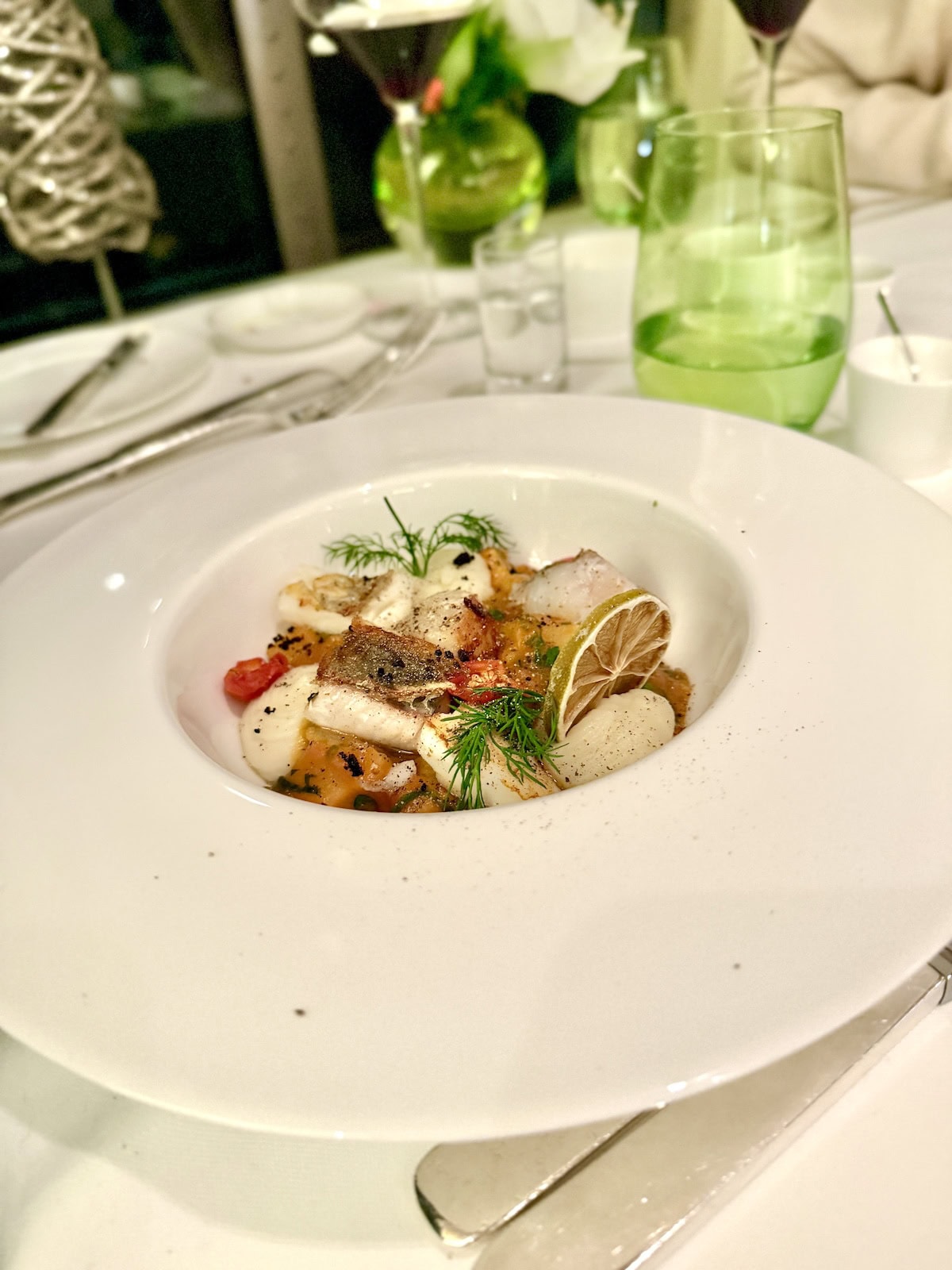 White bowl with fish, tomato, yellow pepper, a lime wheel, and dill.