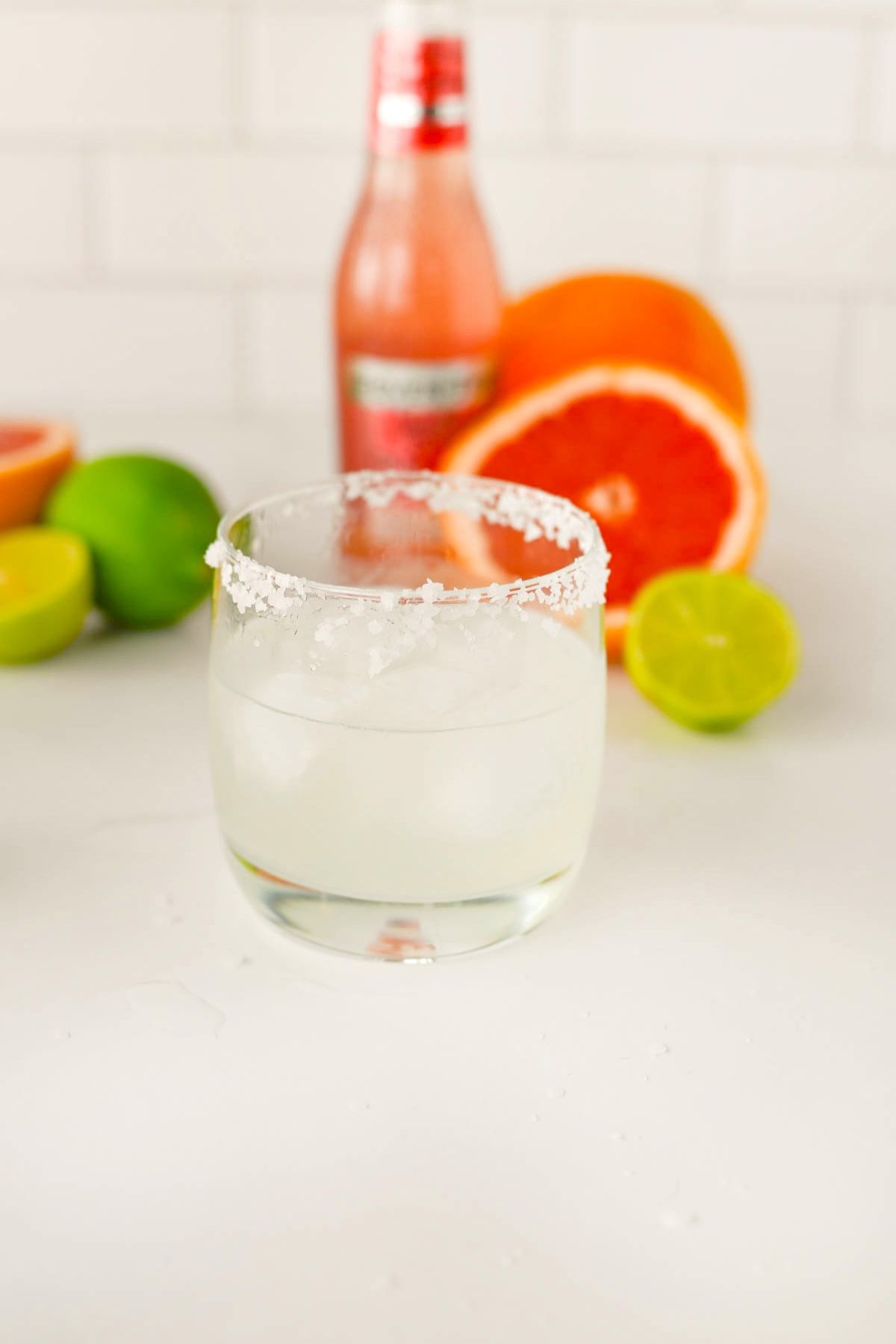 Glass with salt on rim and bottle and fruit in background.