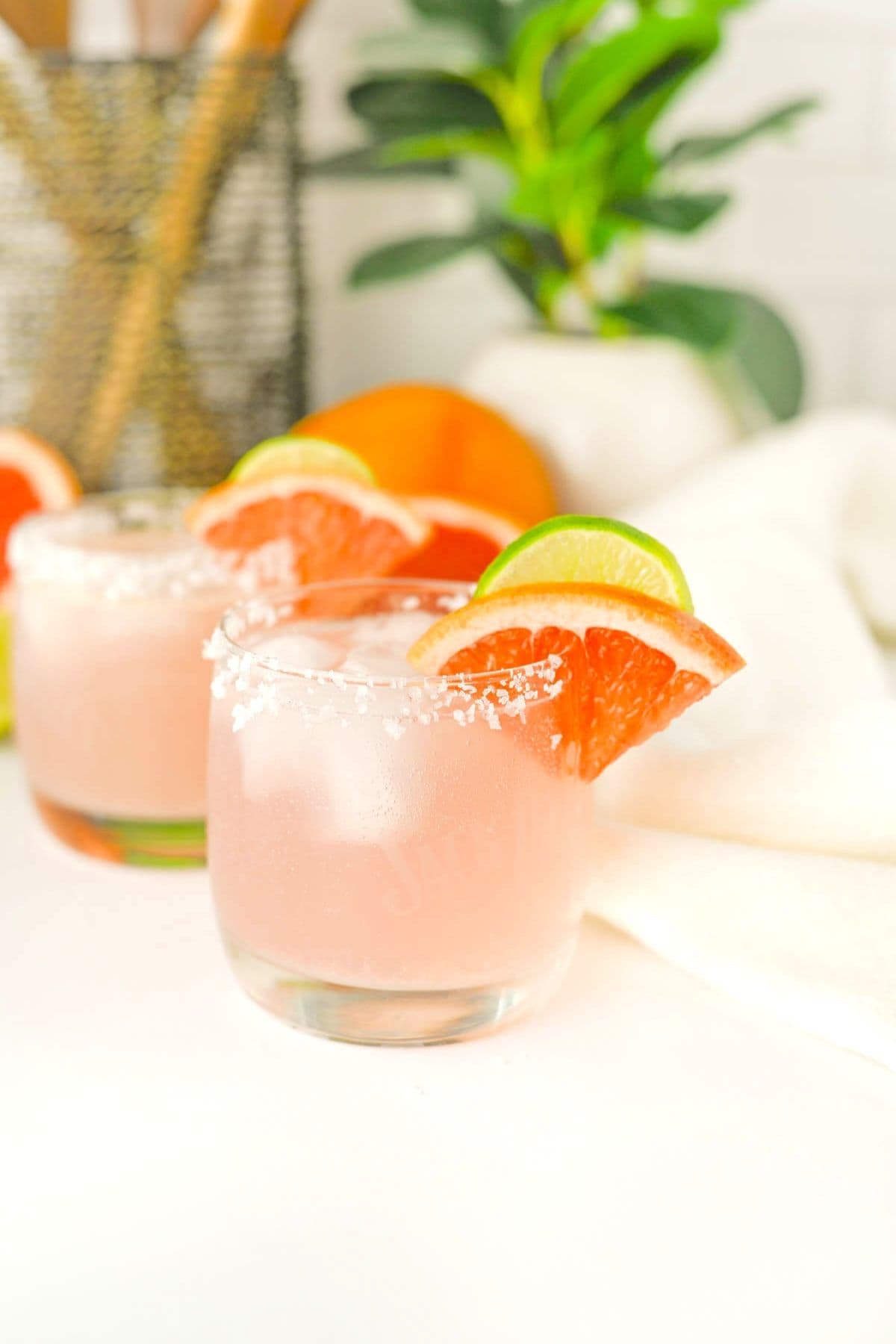 Pink cocktail in a short glass with a salted rim with a piece of grapefruit and lime on rim of glass.