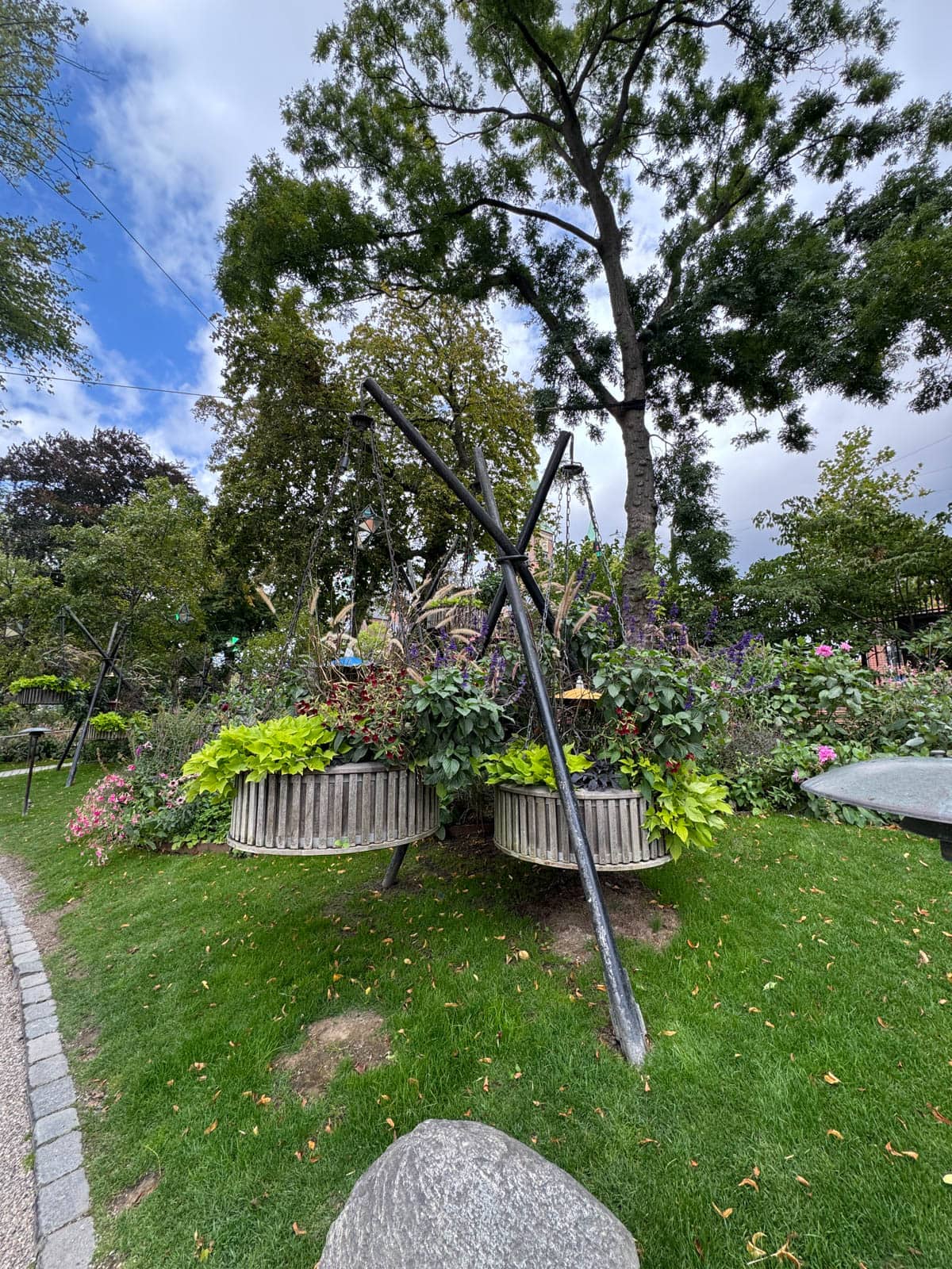 Large hanging pots of freenery with green grass in foreground and trees and bushes in the back.
