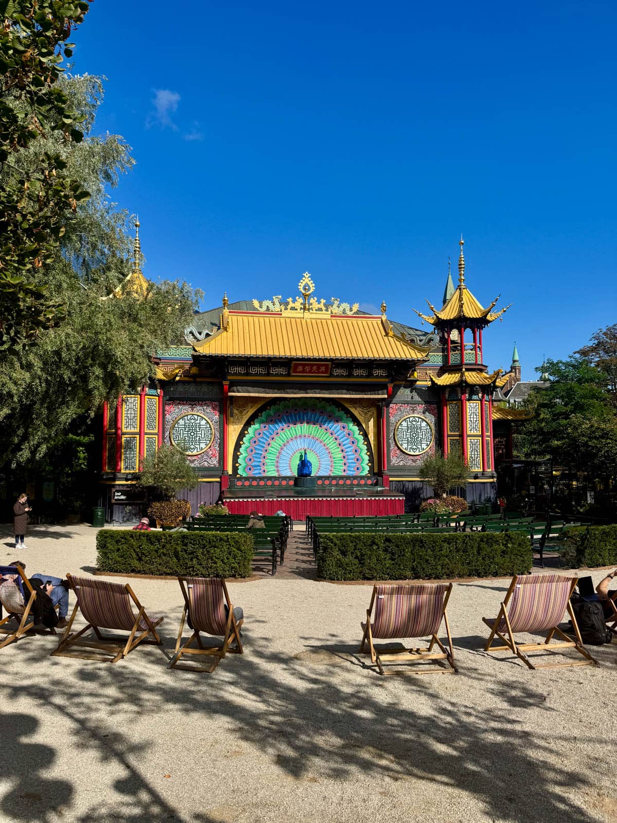 Chinese theater against a blue sky with benches in front and folding chairs in back.