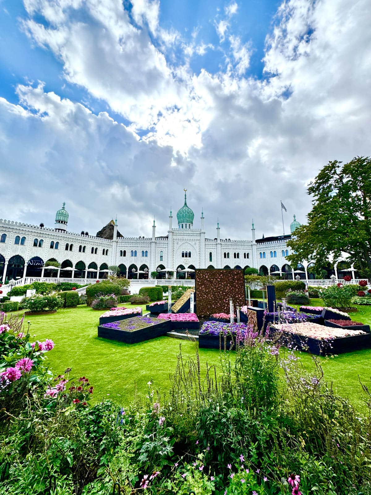 White Moorish-style building against a cloudy blue sky with gardens in front.