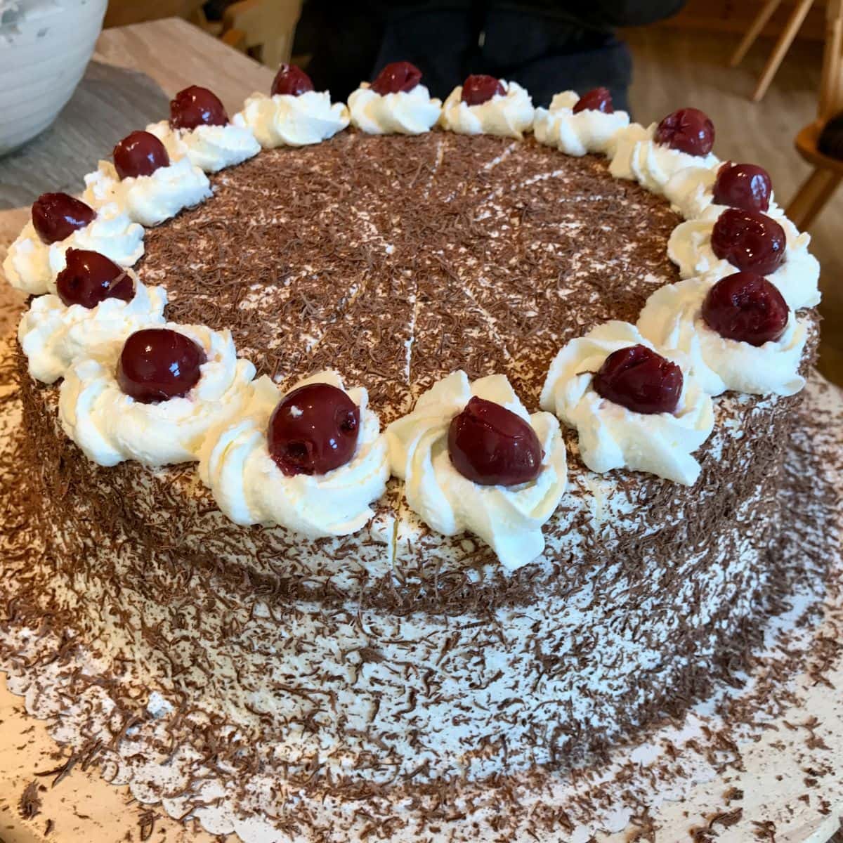Black Forest cake covered in shaved chocolate with whipped cream and cherries on top.