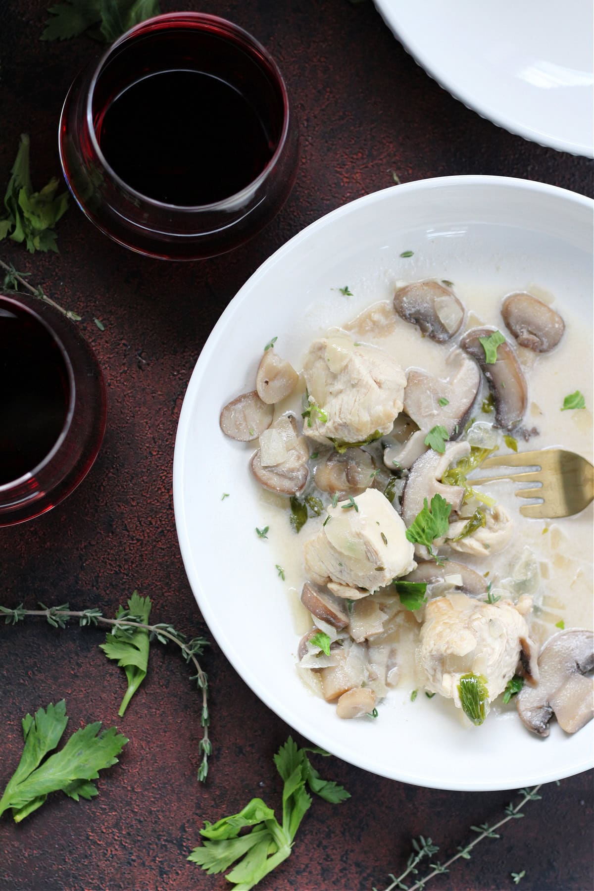 Chicken and mushrooms in a white broth in a white bowl.