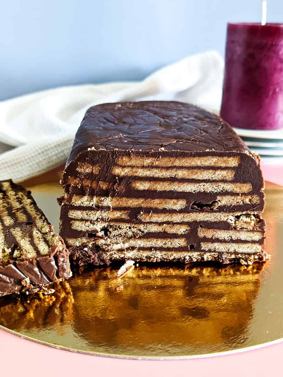Layered chocolate and biscuit cake on a gold platter on a pink counter.