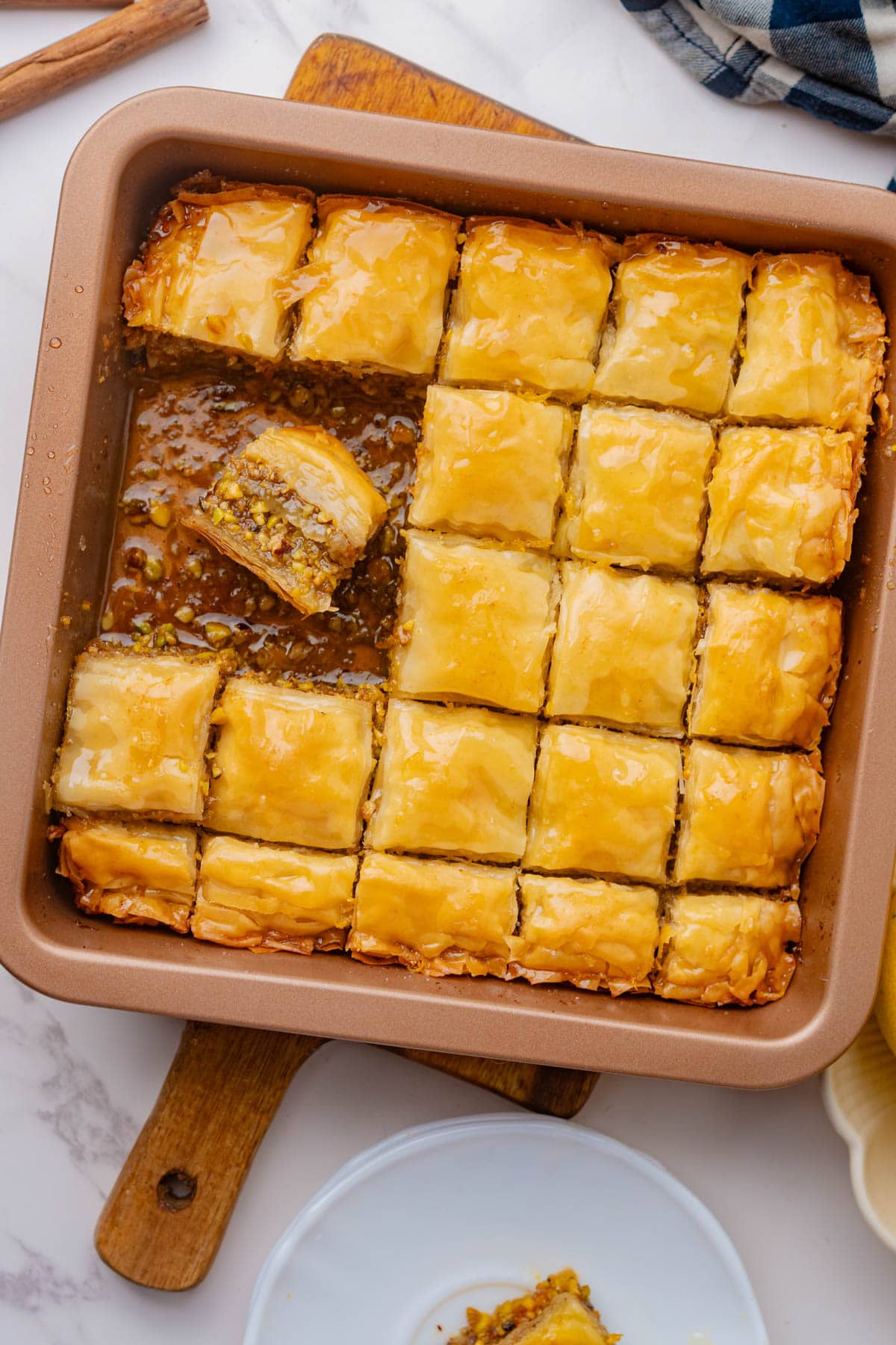 Baking dish of baklava cut into squares with pieces missing and one piece turned sideways laying in syrup at bottom.