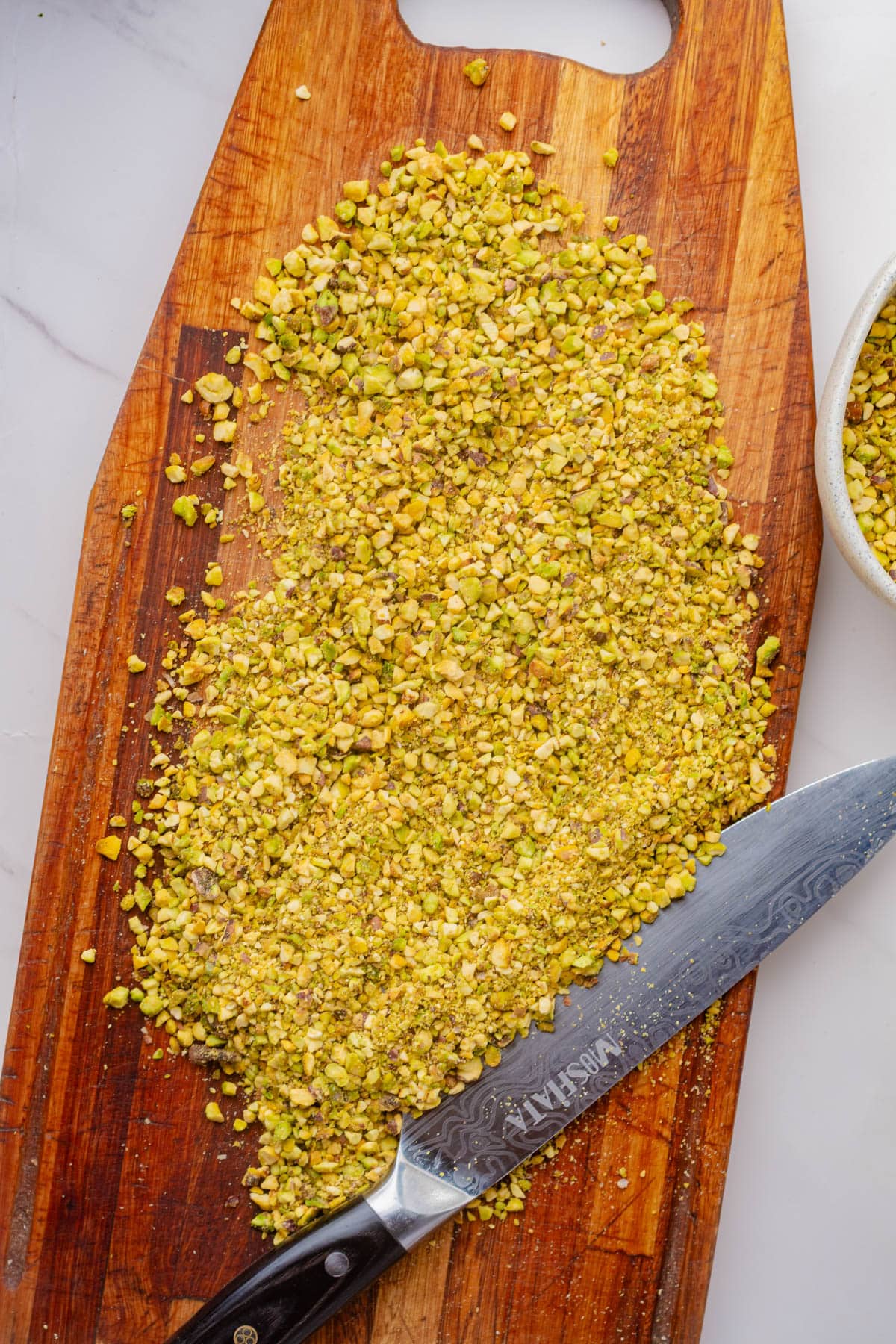 Chopped pistachio nuts on a wood board with a knife.