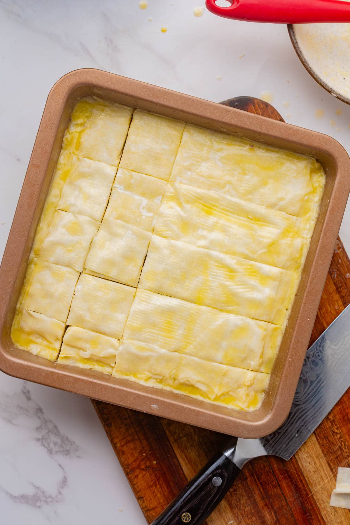 Unbaked phyllo dough in a square pan topped with melted butter.