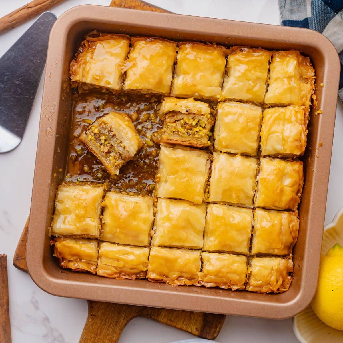Baking dish of baklava cut into squares with pieces missing and one piece turned sideways laying in syrup at bottom.