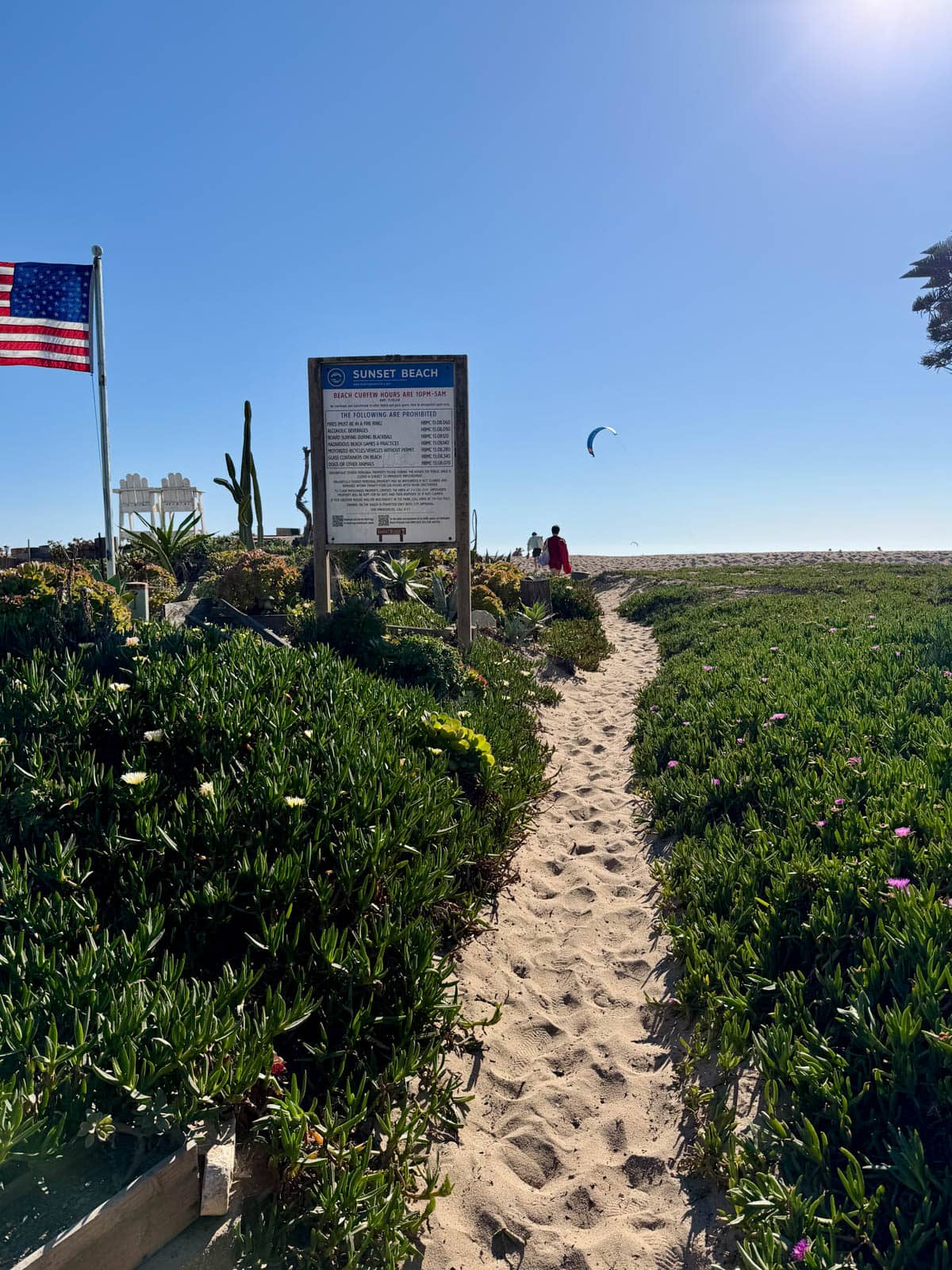 Sand path at sunset beach with sign and American flag.