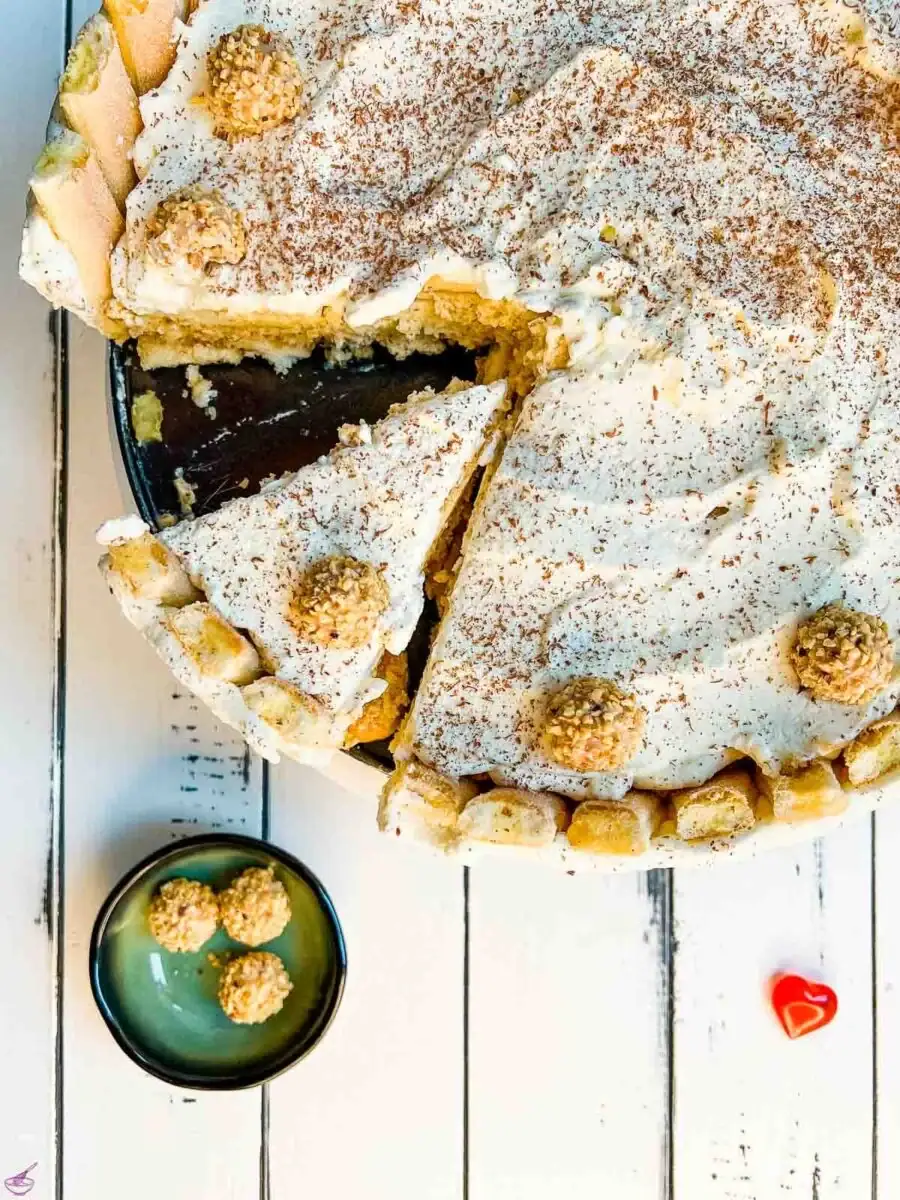 Torte with ladyfingers, nuts, and whipped topping on a white table.