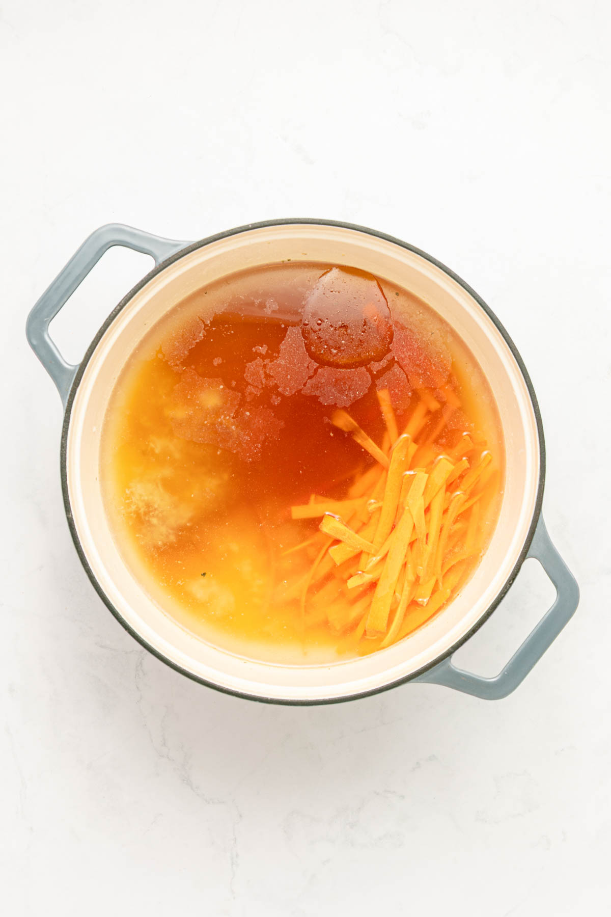 Chicken broth in a pot with carrots.