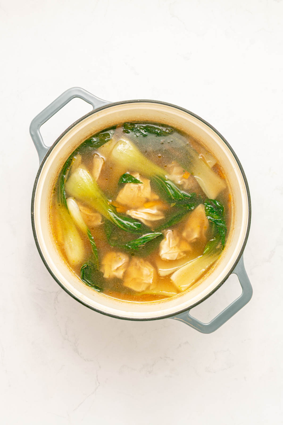 Chicken broth in a pot with carrots and wontons.