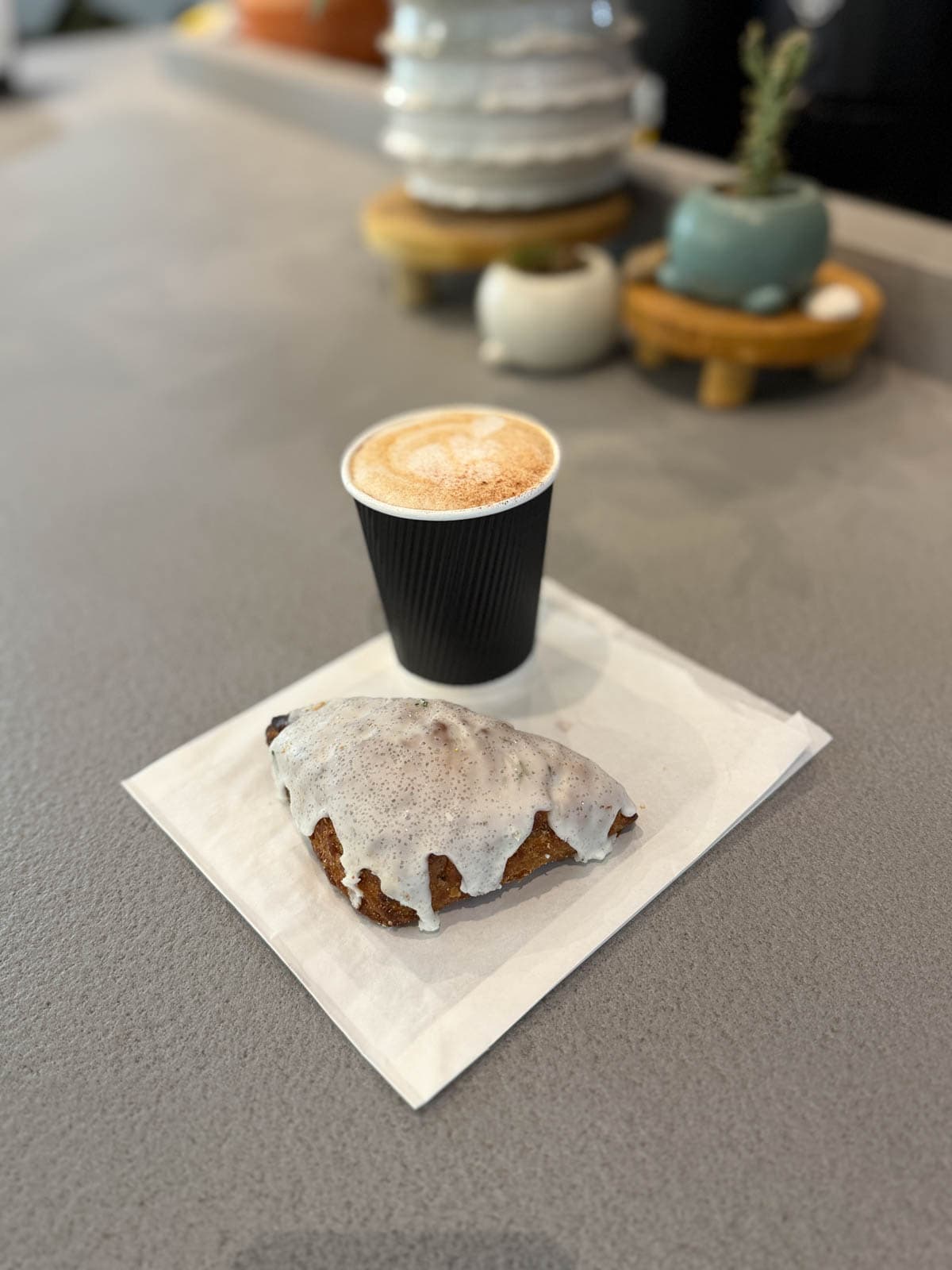 Cappuccino  with an iced scone on a flattened white bag.
