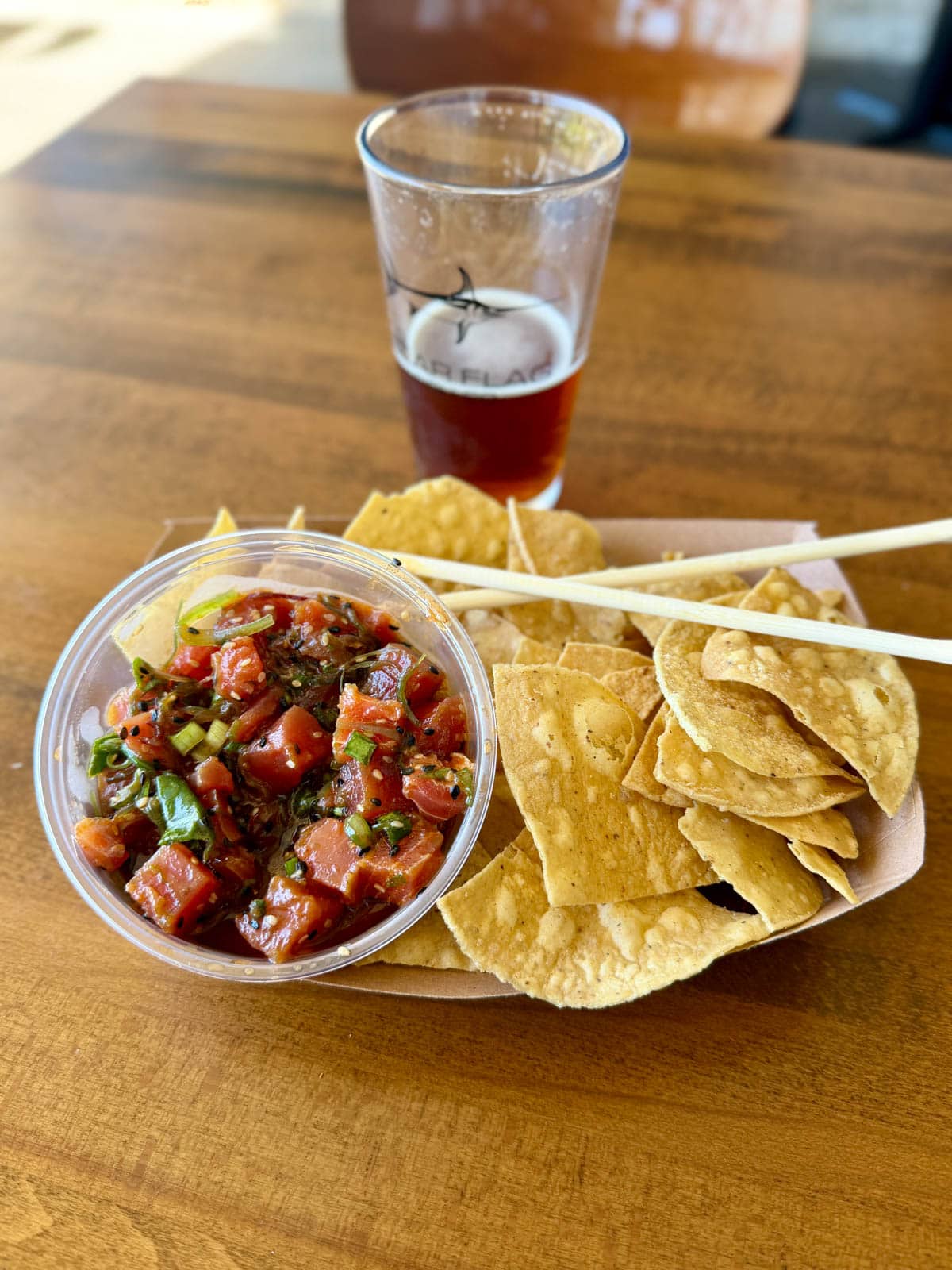 Tuna poke in a bowl with tortilla chips with a beer in the background.