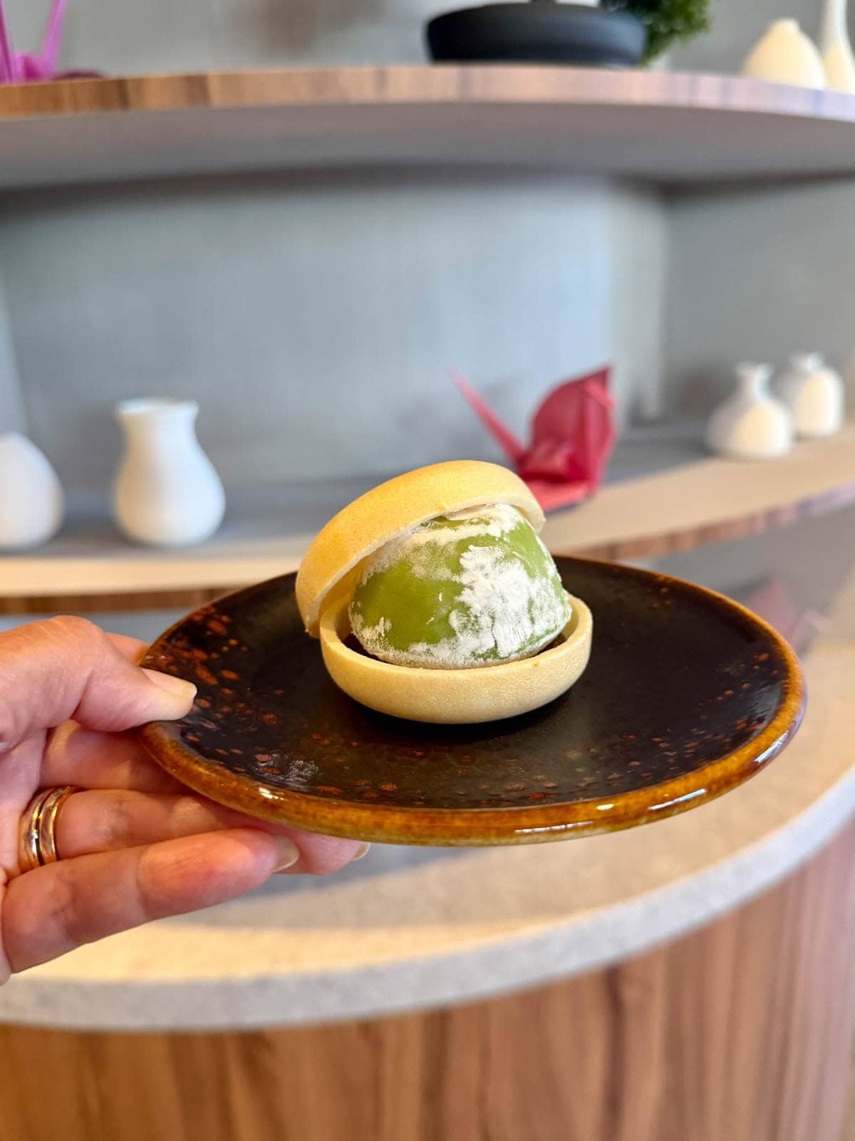 Hand holding a black and brown plate of mochi ice cream.