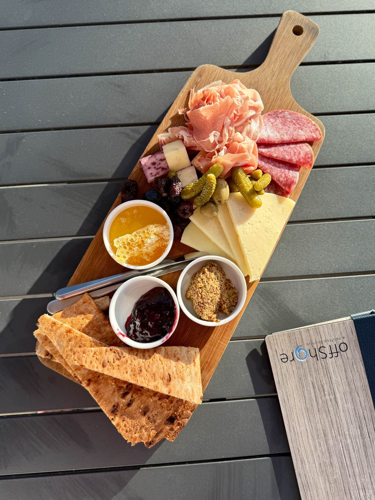 Wood board with charcuterie, crackers, cheese, pickles, and sauces on balck table.
