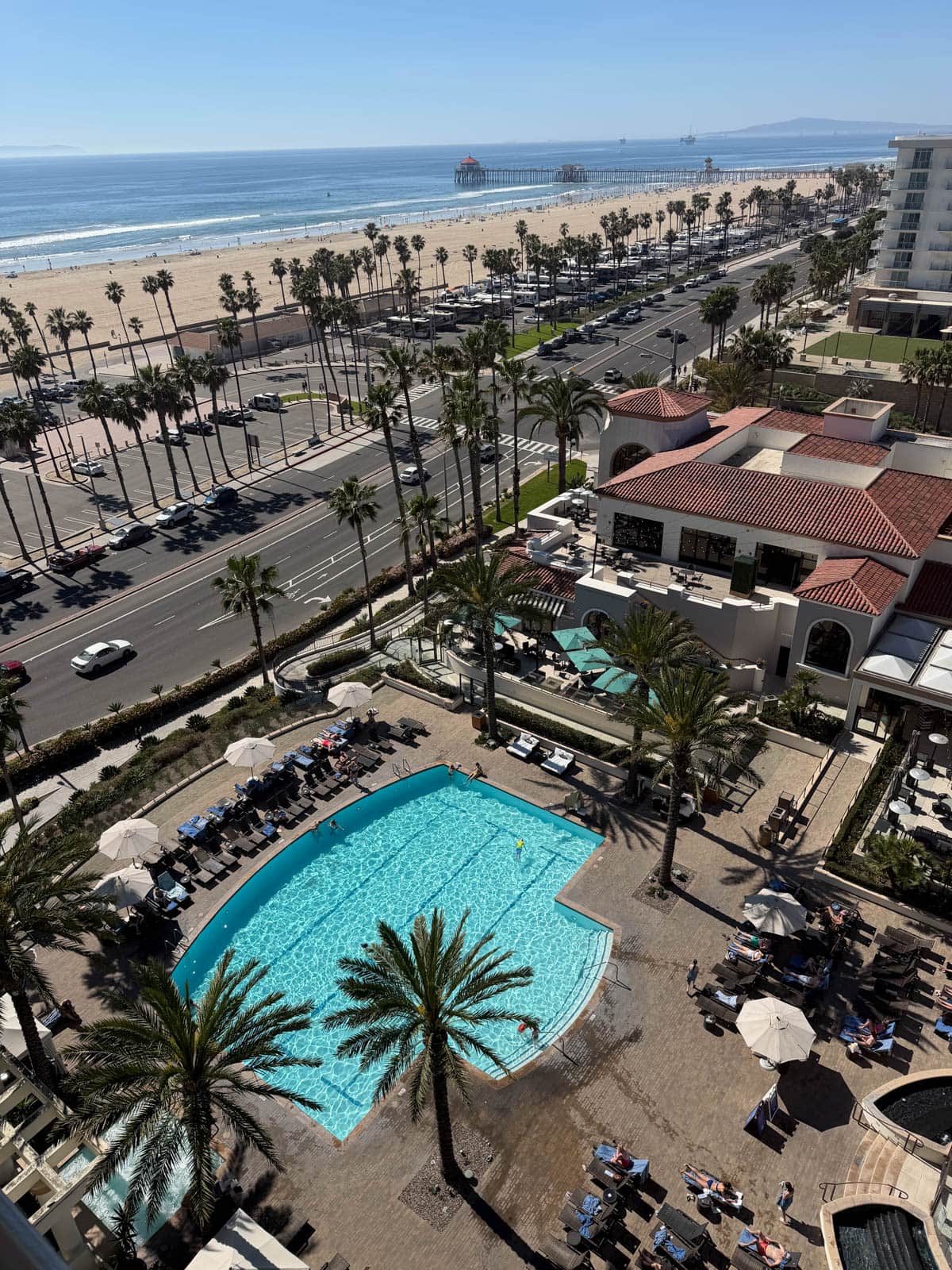 View of a pool and the beach from a hotel balcony.
