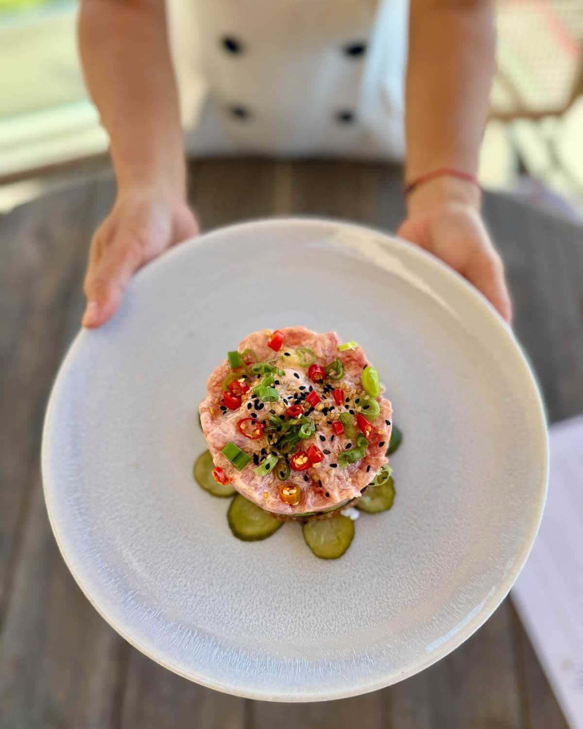 Hands holding a tuna appetizer layered over pickles on a white plate.