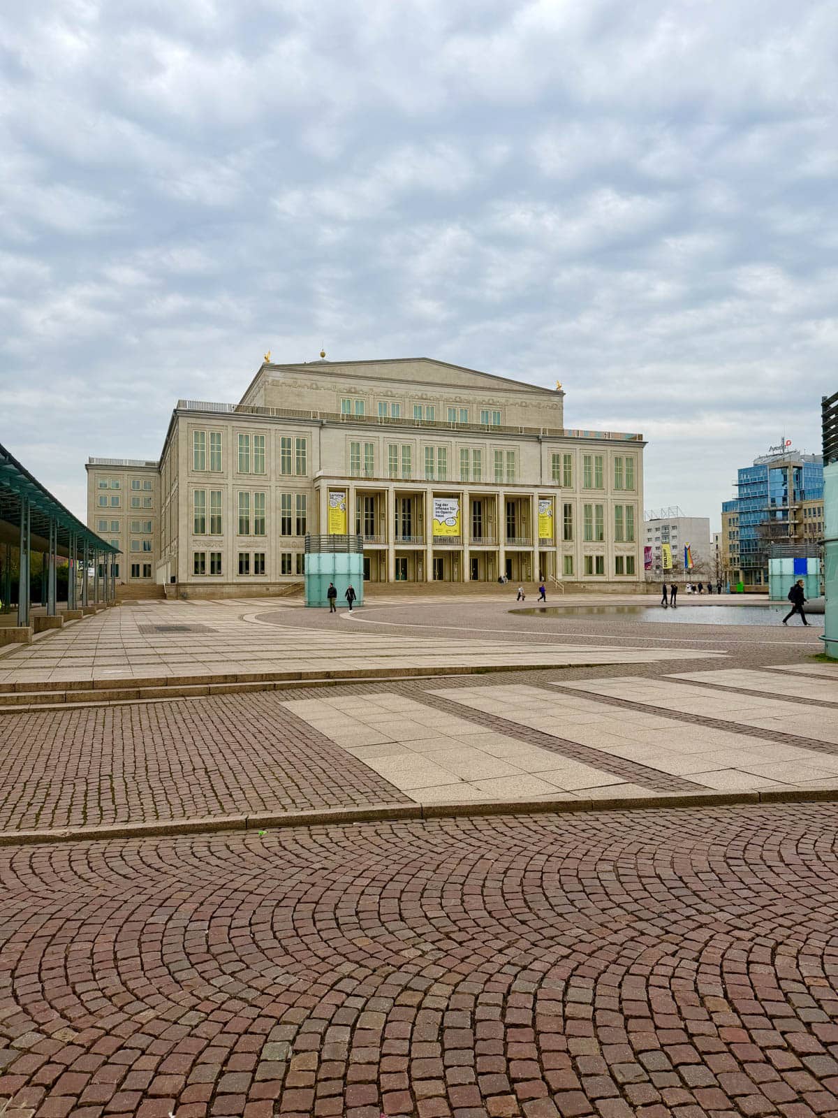 Historic building with circle of pool of water in front and people walking around.