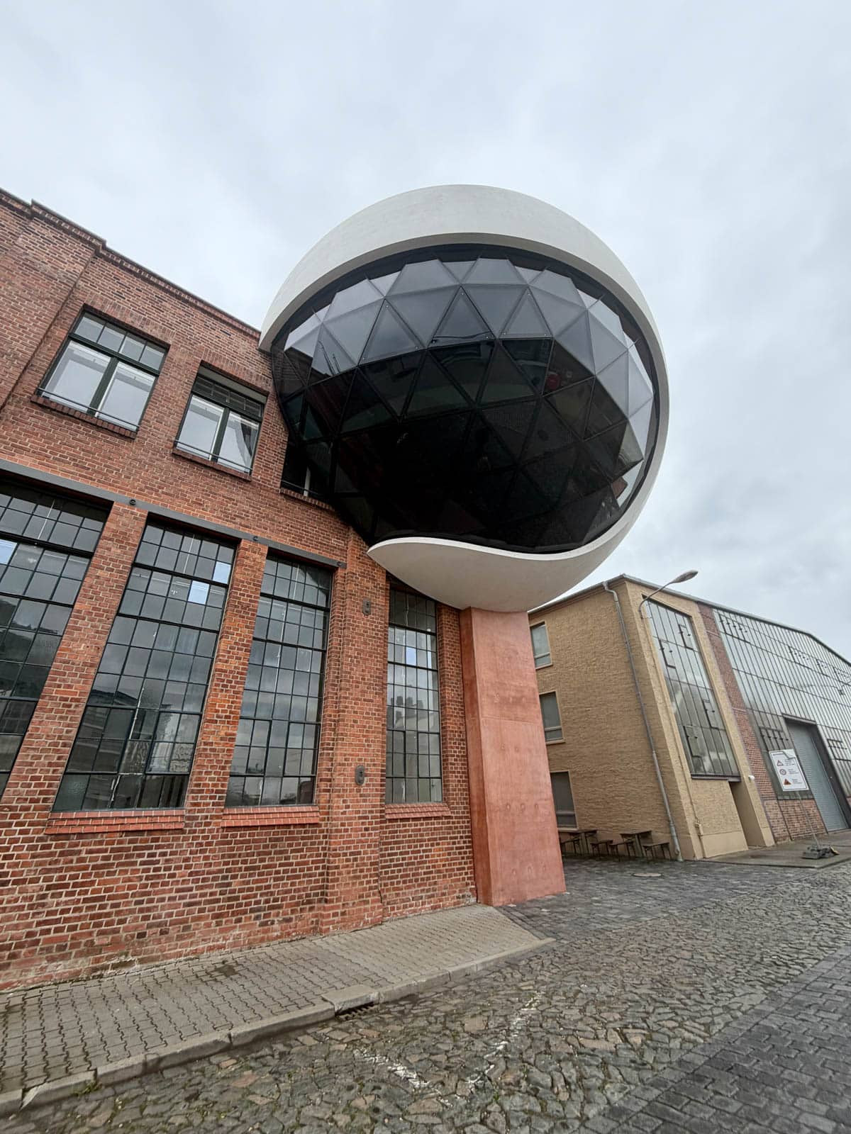 Structure resembling an eyeball attached to a historic brown stone building.