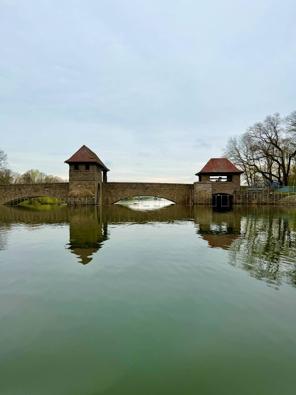Bridge with two short towers over river with trees in background.
