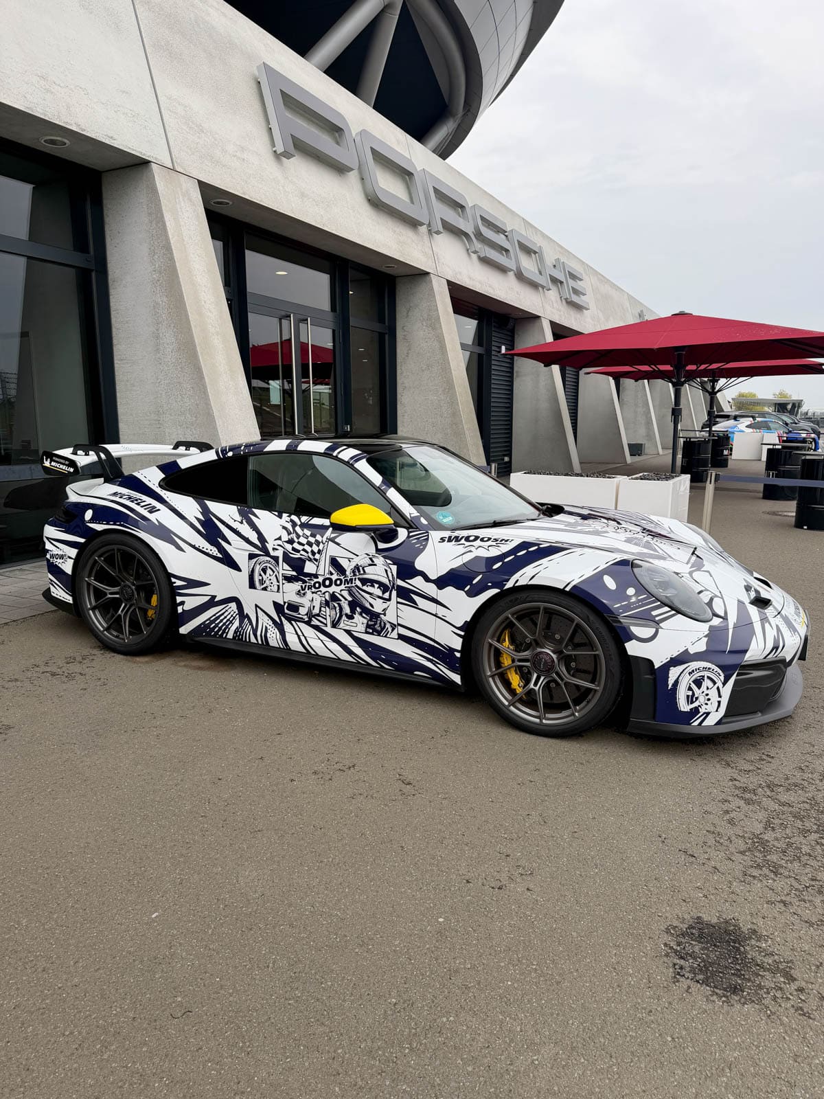 Porsche with graphic design in front of factory.