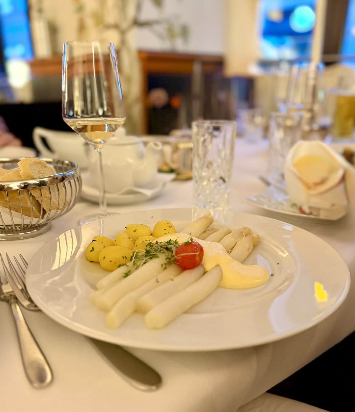 White plate with white asparagus, potatoes, and hollandaise sauce.