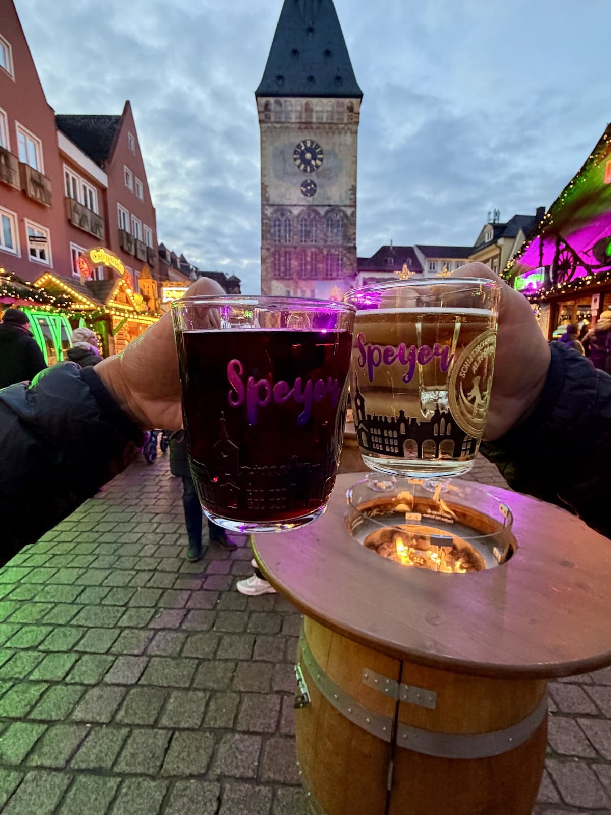 Two hands holding glass mugs filled with gluhwein over a fire pit at a Christmas market in Germany.