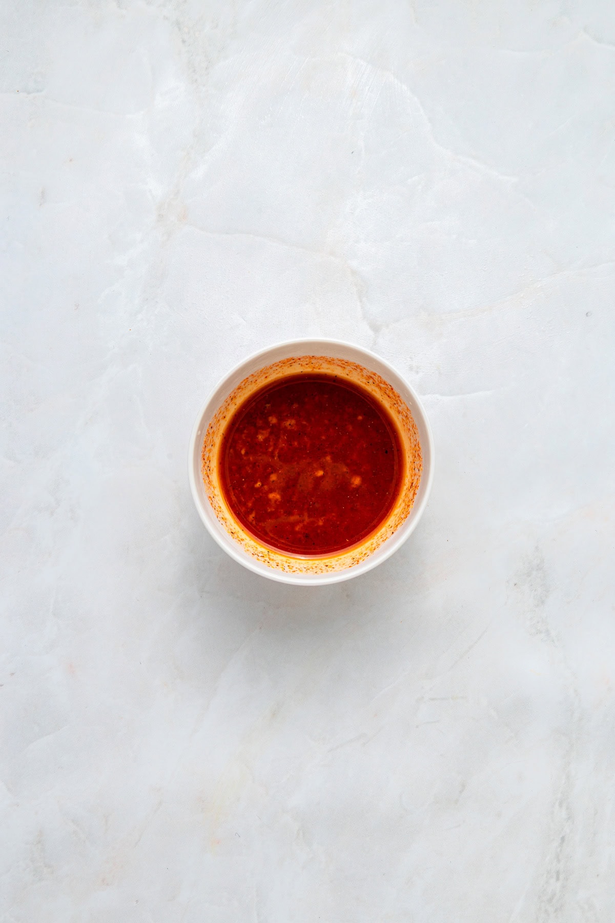 Ingredients for marinade for chicken stirred together in a small white bowl on a white counter.