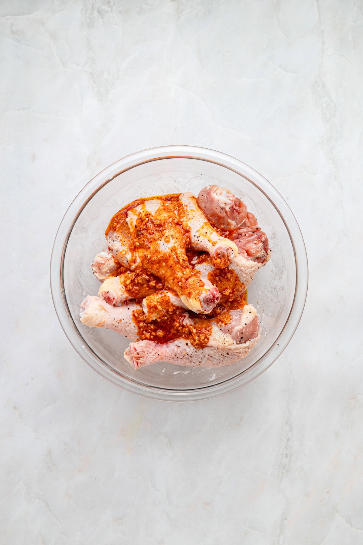 Marinade poured over chicken in a glass bowl on a white counter.