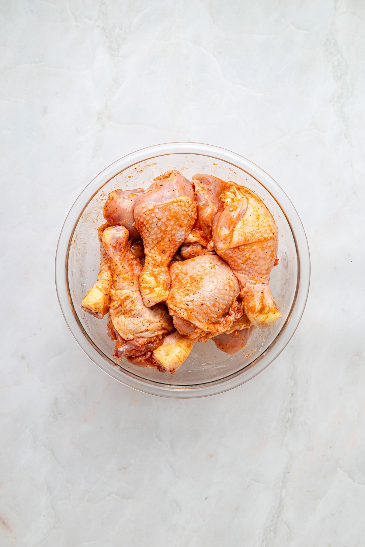 Marinade rubbed into chicken in a glass bowl on a white counter.