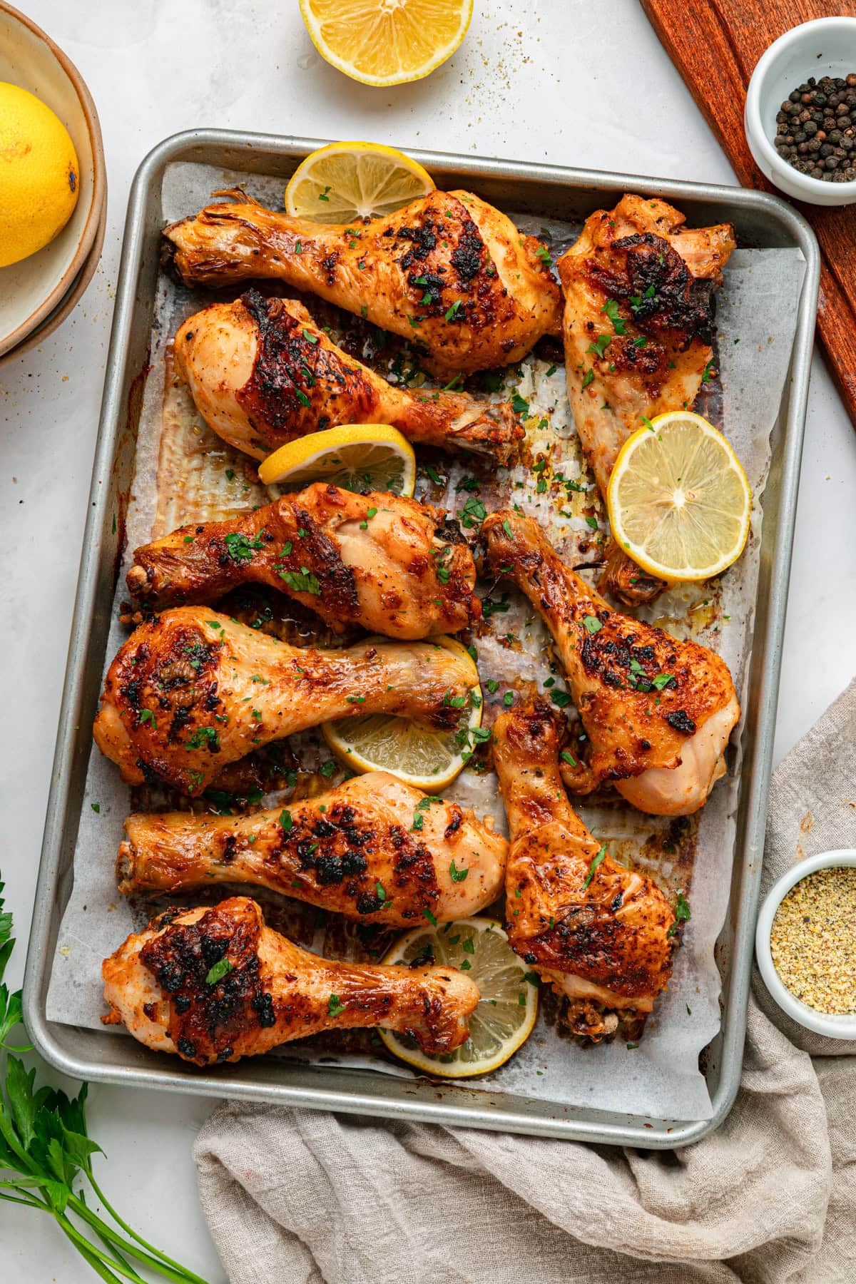 Cooked chicken drumsticks with lemon slices and fresh parsley on a baking sheet.