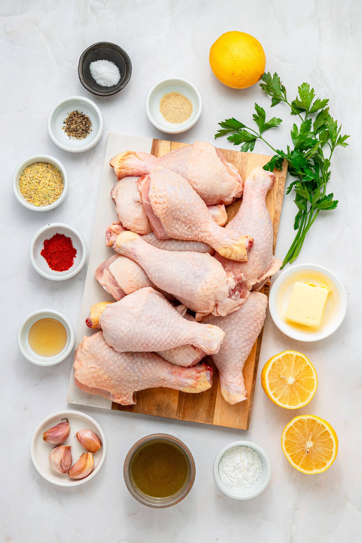 Raw chicken drumsticks on a cutting board surrounded by ingredients and spices to make lemon chicken.