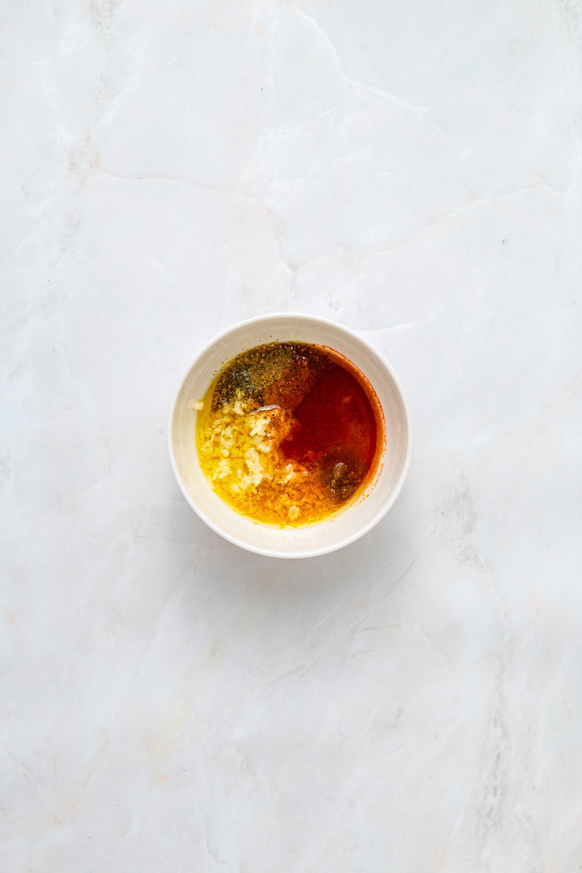 Ingredients for marinade for chicken in a small white bowl on a white counter.